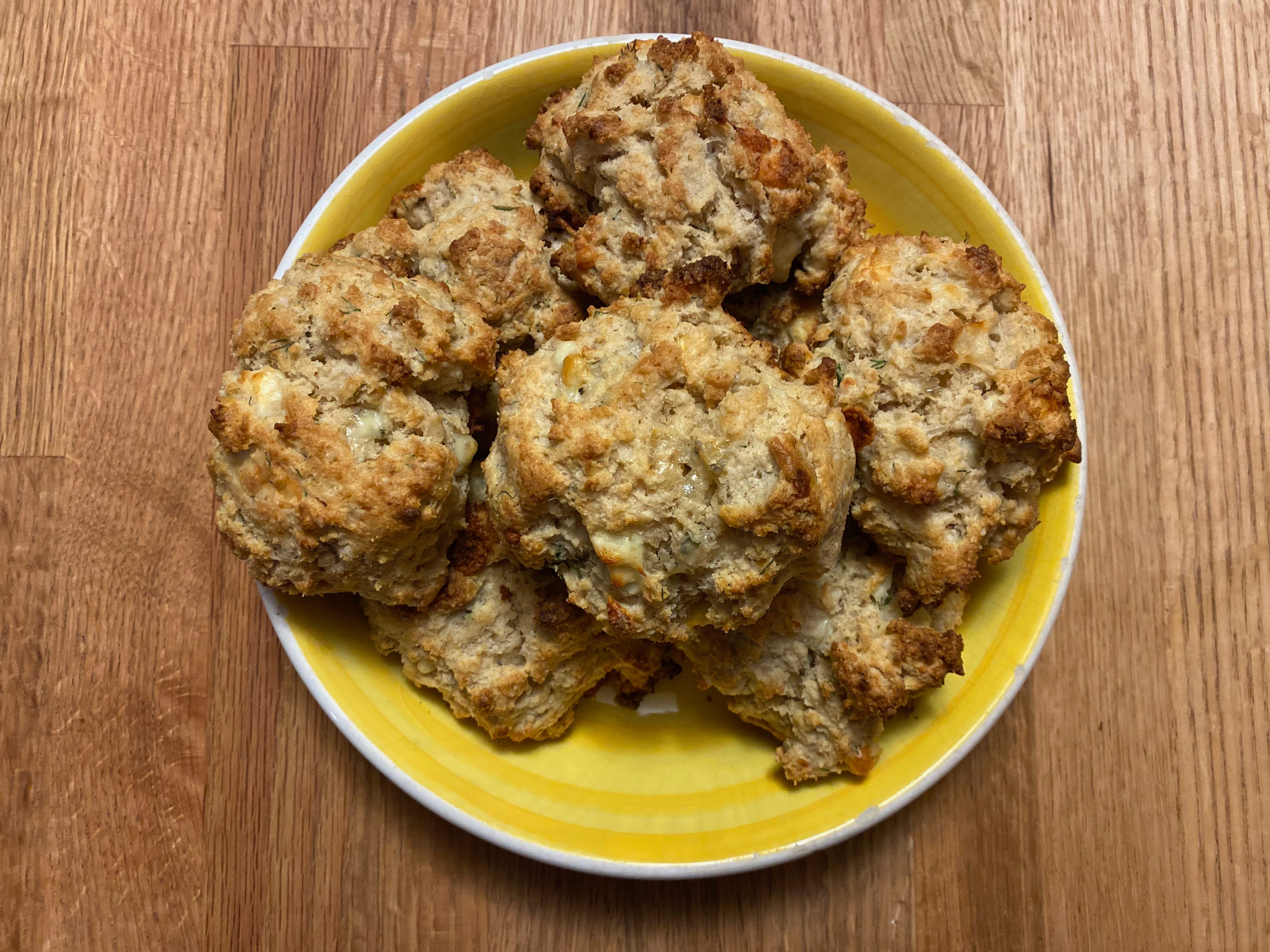 A pile of golden brown biscuits in a yellow ceramic bowl on a wooden counter.