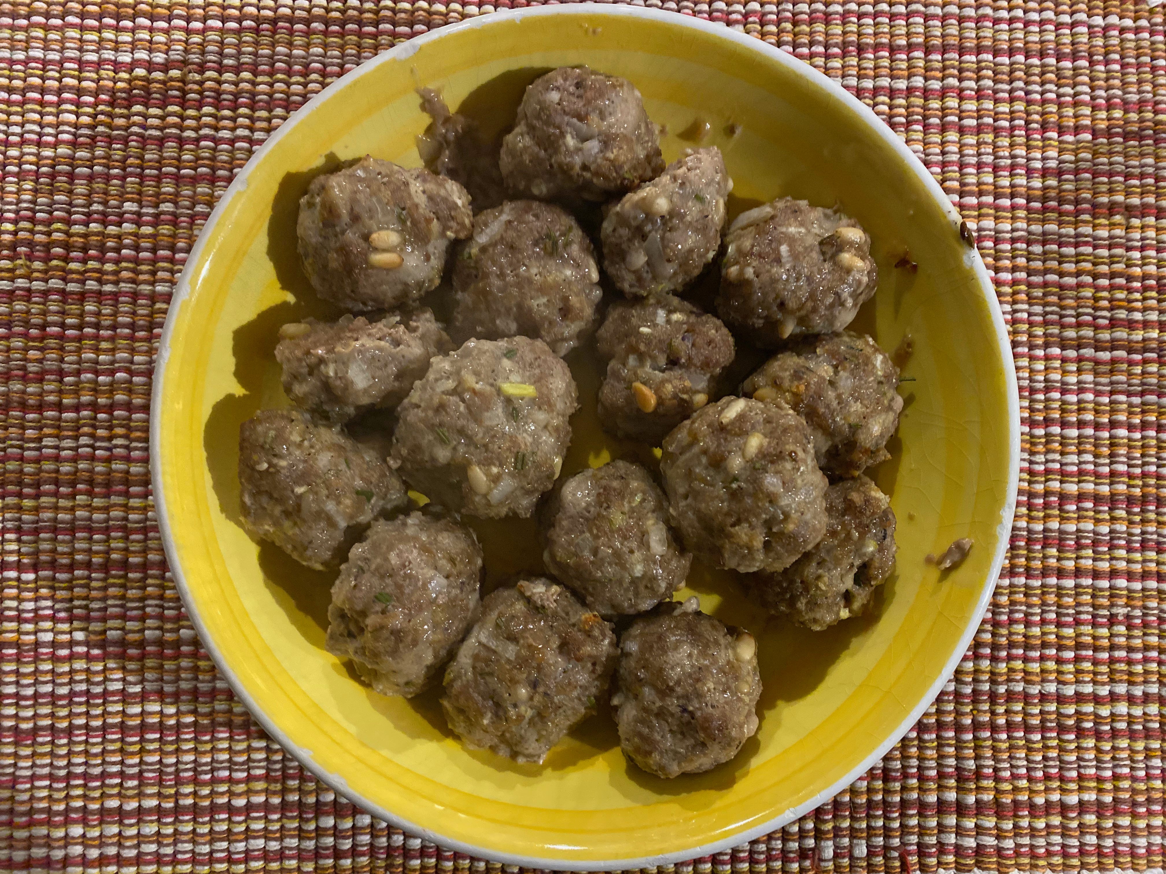 A shallow yellow bowl full of browned meatballs sits on a red, white and orange woven placemat.