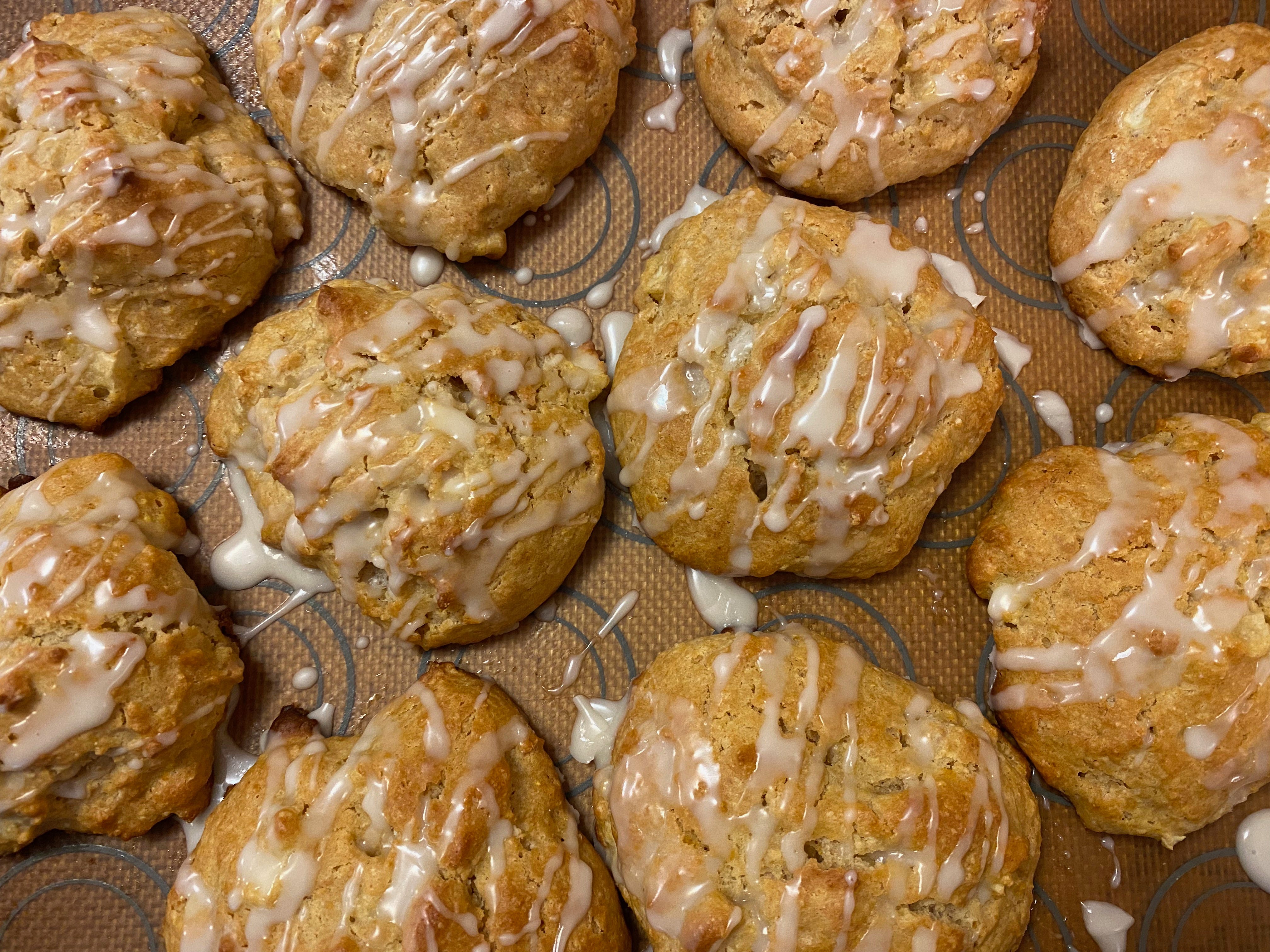 Closeup of ten round scones, drizzled with white icing, on a baking tray.