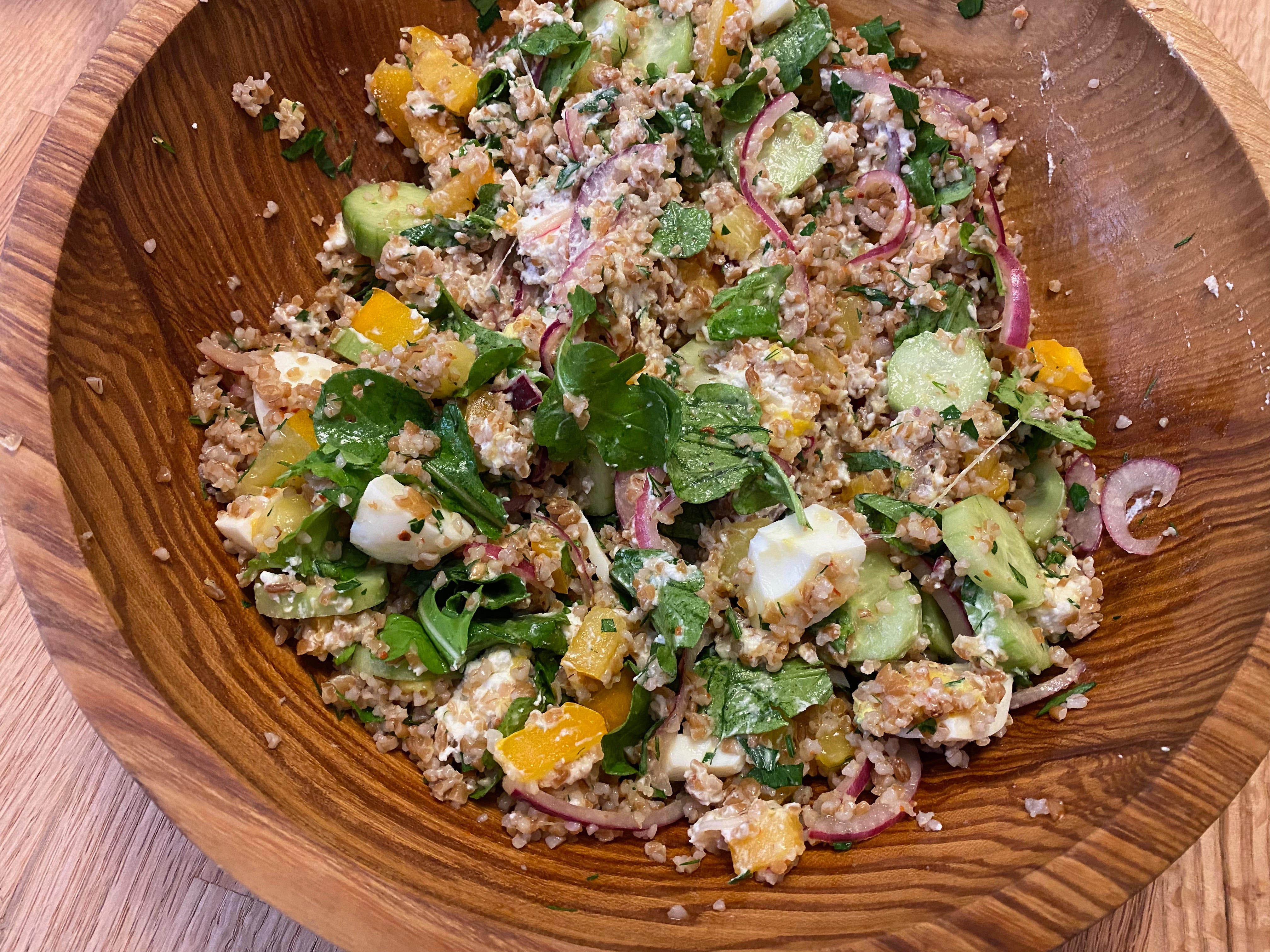 Close up of a wooden bowl filled with a bulgar, tomato, argula, and pickled onion salad.