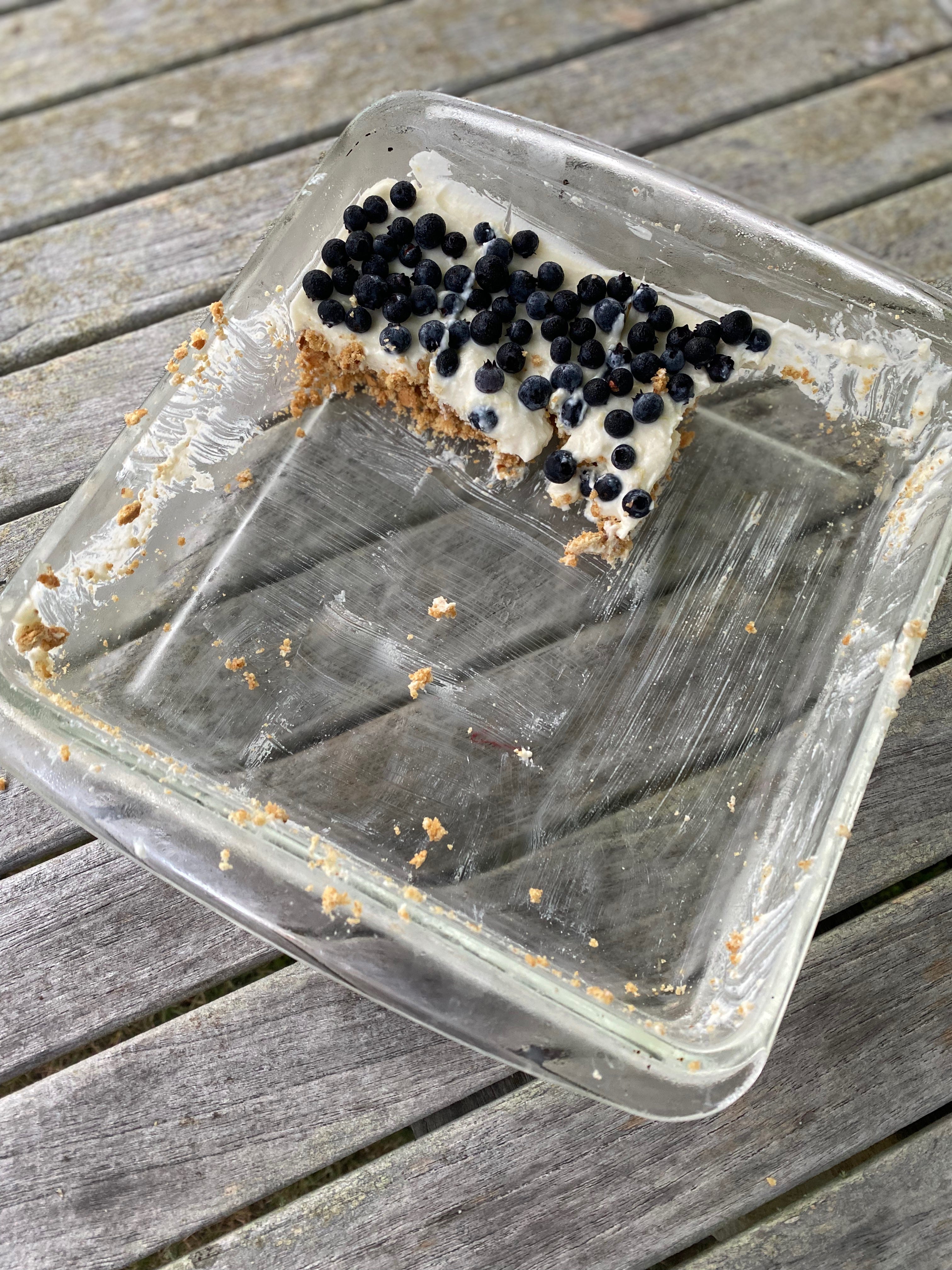 A mostly-empty glass baking dish holding three cheesecake bars topped with fresh blueberries.