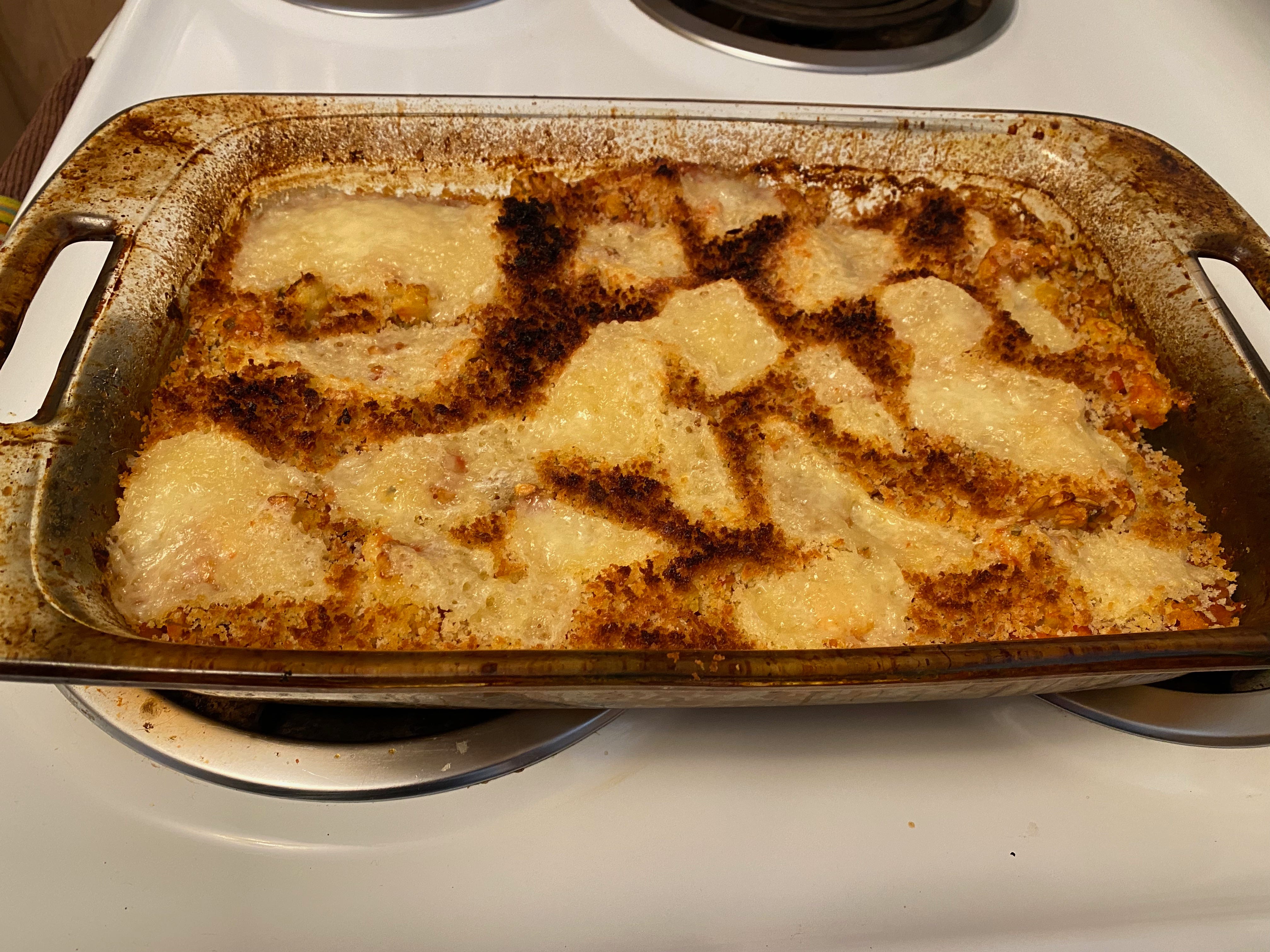 A glass 9x13-inch casserole dish filled with browned bread crumbs and bubbly cheese sits on a stovetop.