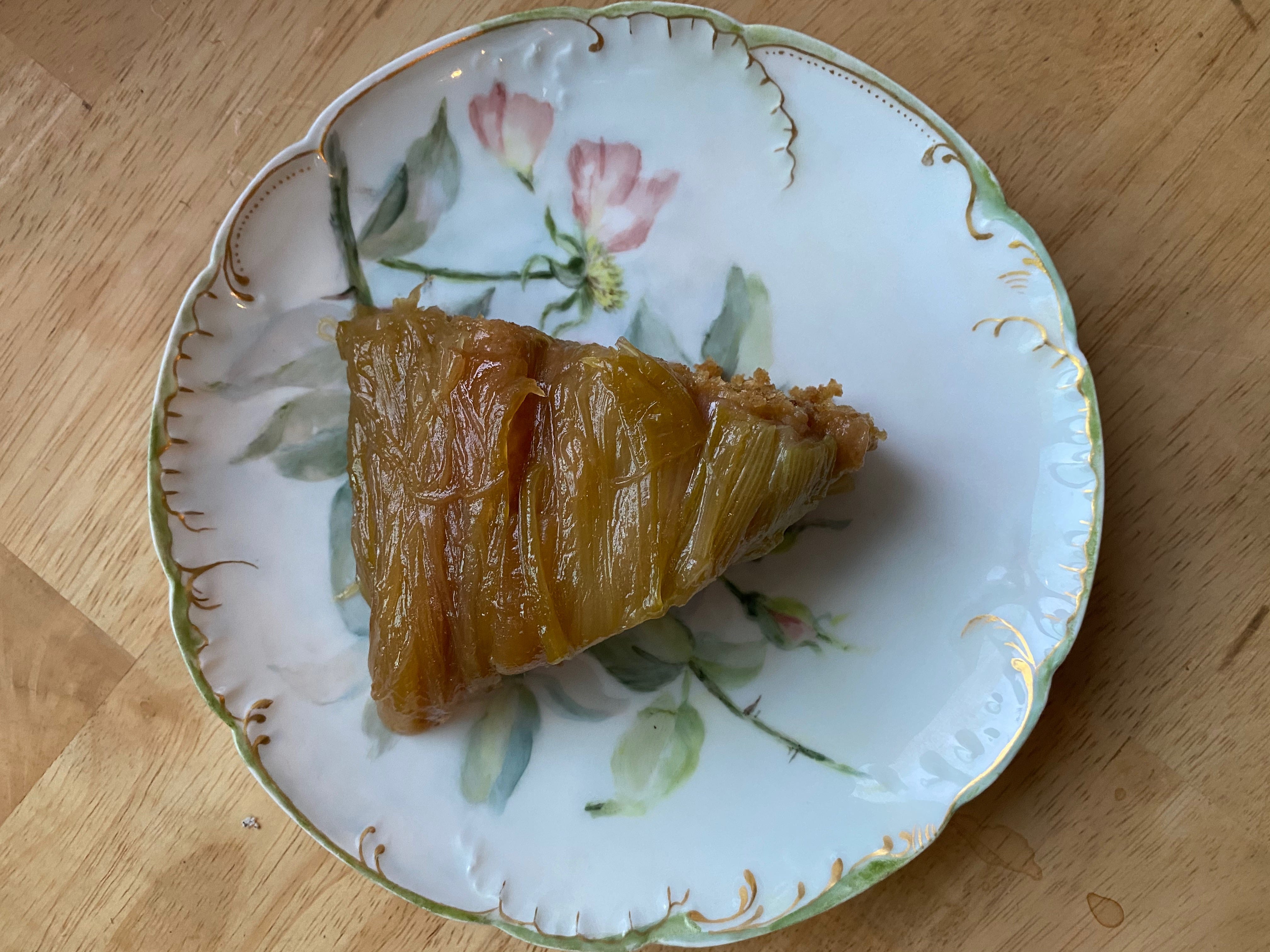 A slice of rhubarb upside-down cake on a china plate painted with flowers.