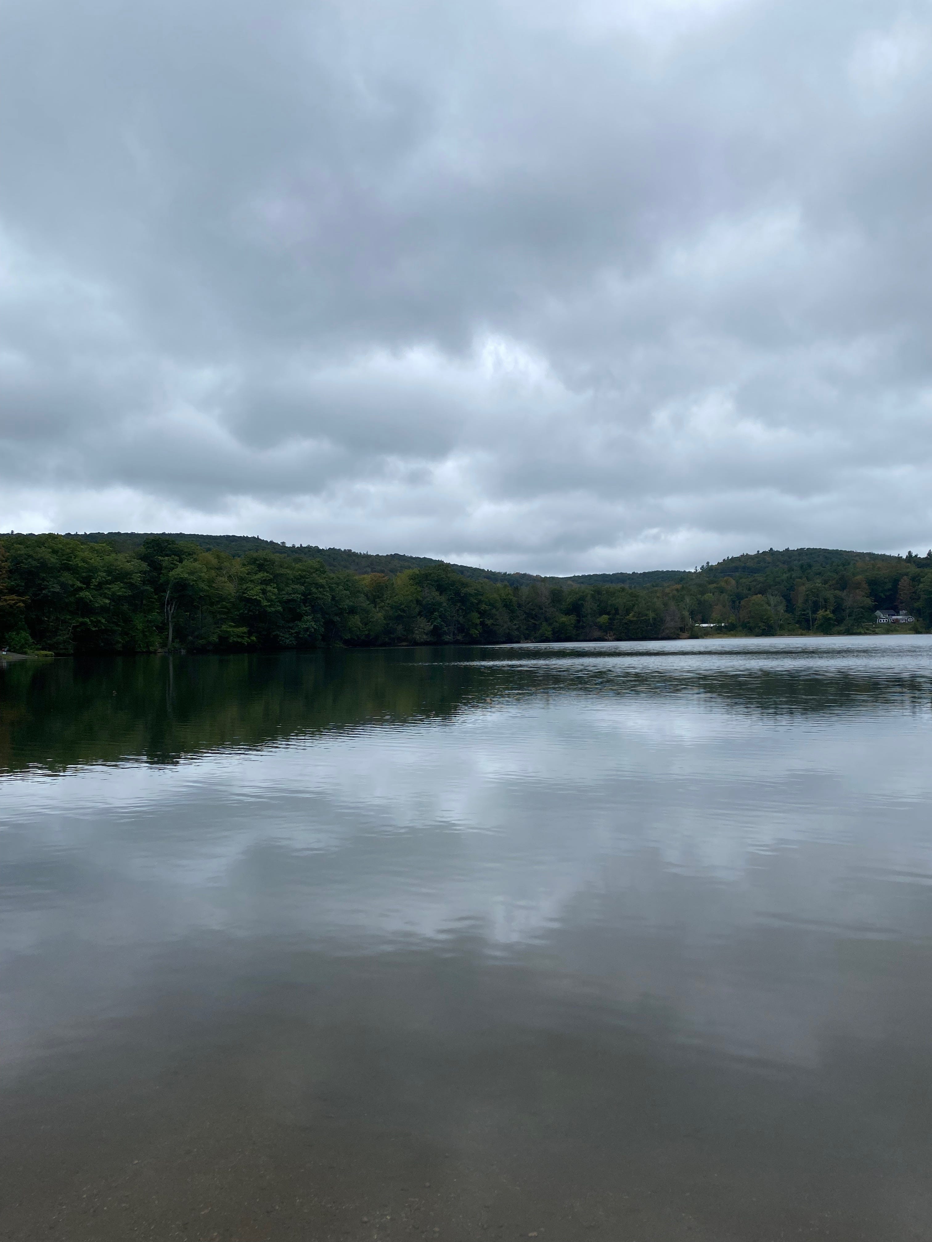 Ashfield Lake on a grey day, the sky full of silver clouds, reflected in the still water.