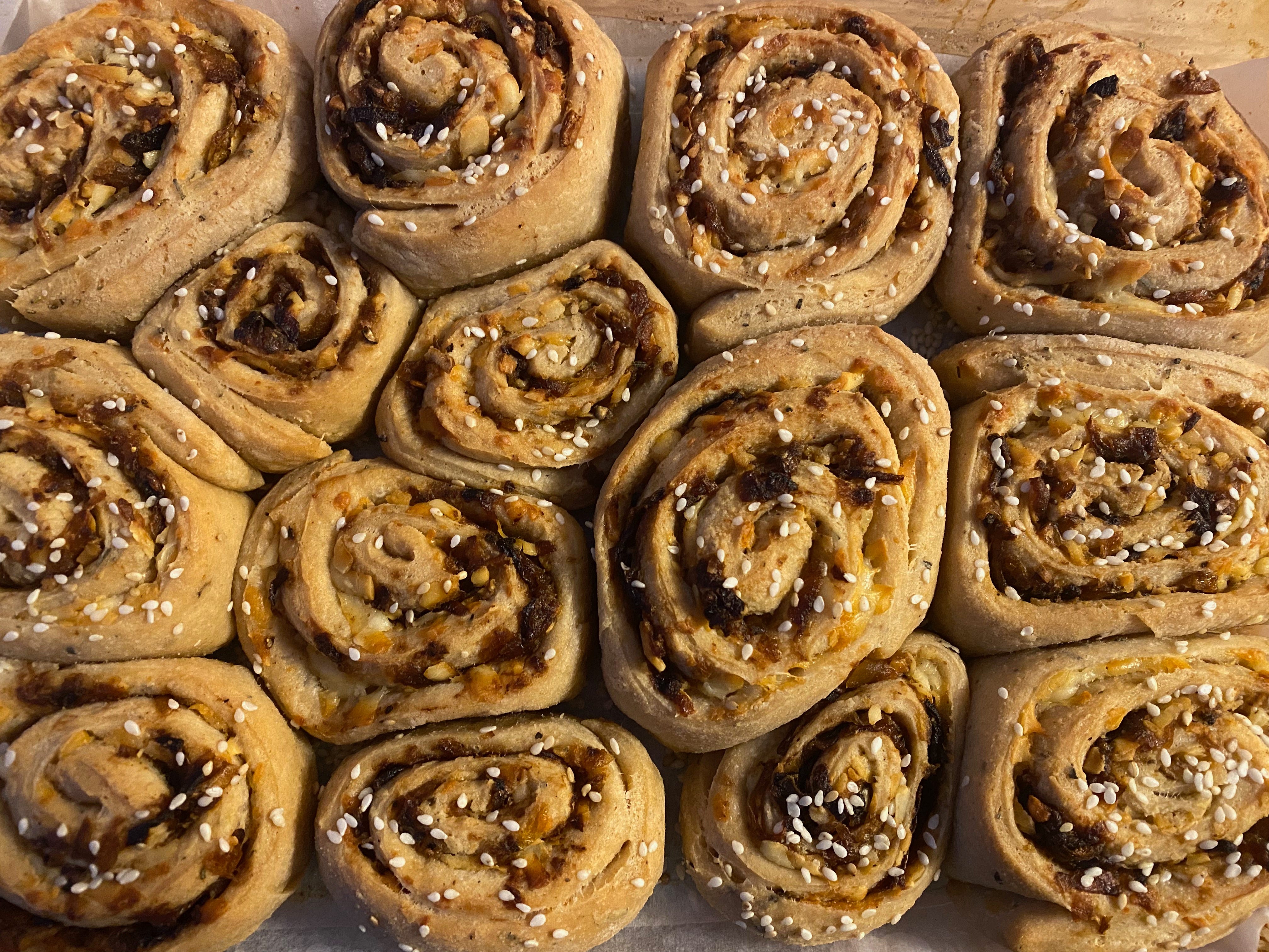 A closeup of a pan of round swirl buns filled with caramelized onions and topped with sesame seeds.