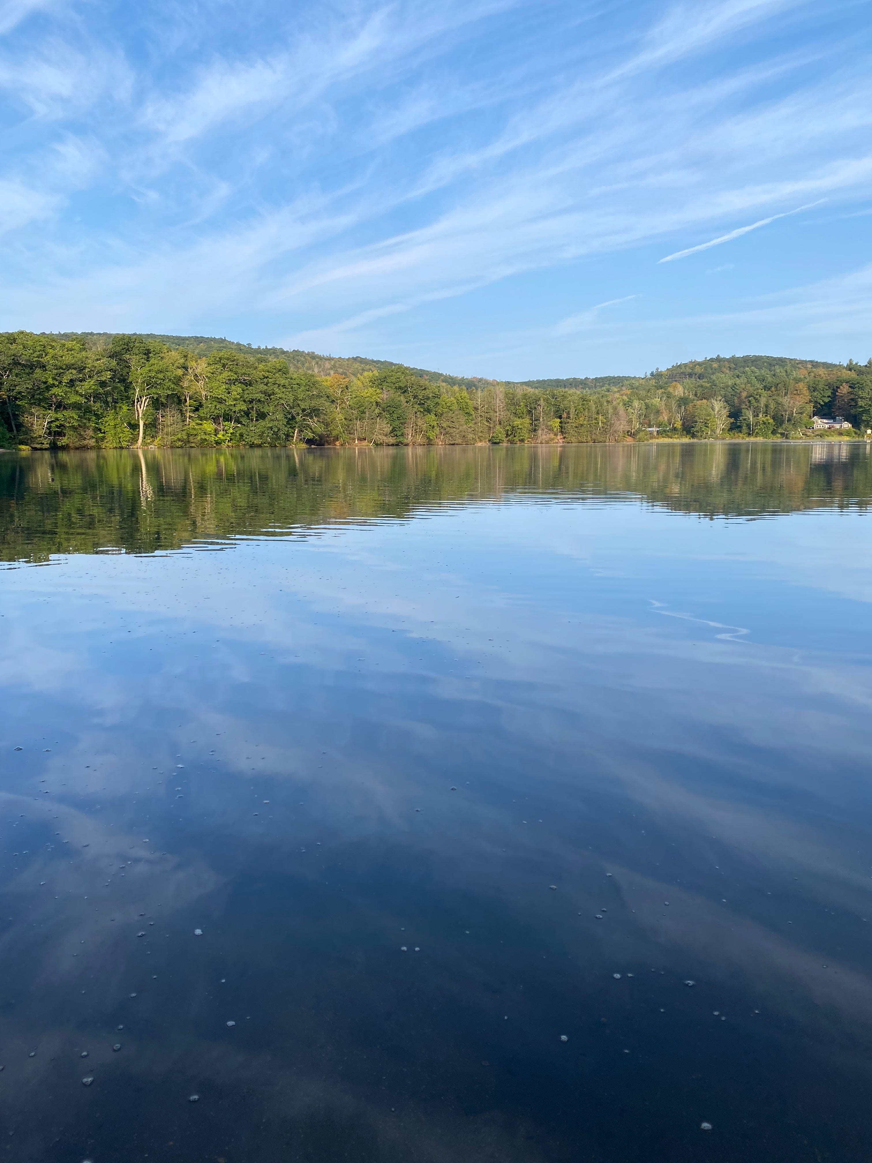 Ashfield Lake, with a cloud-streaked sky reflected in the still water, and tree-covered hills in the background. 