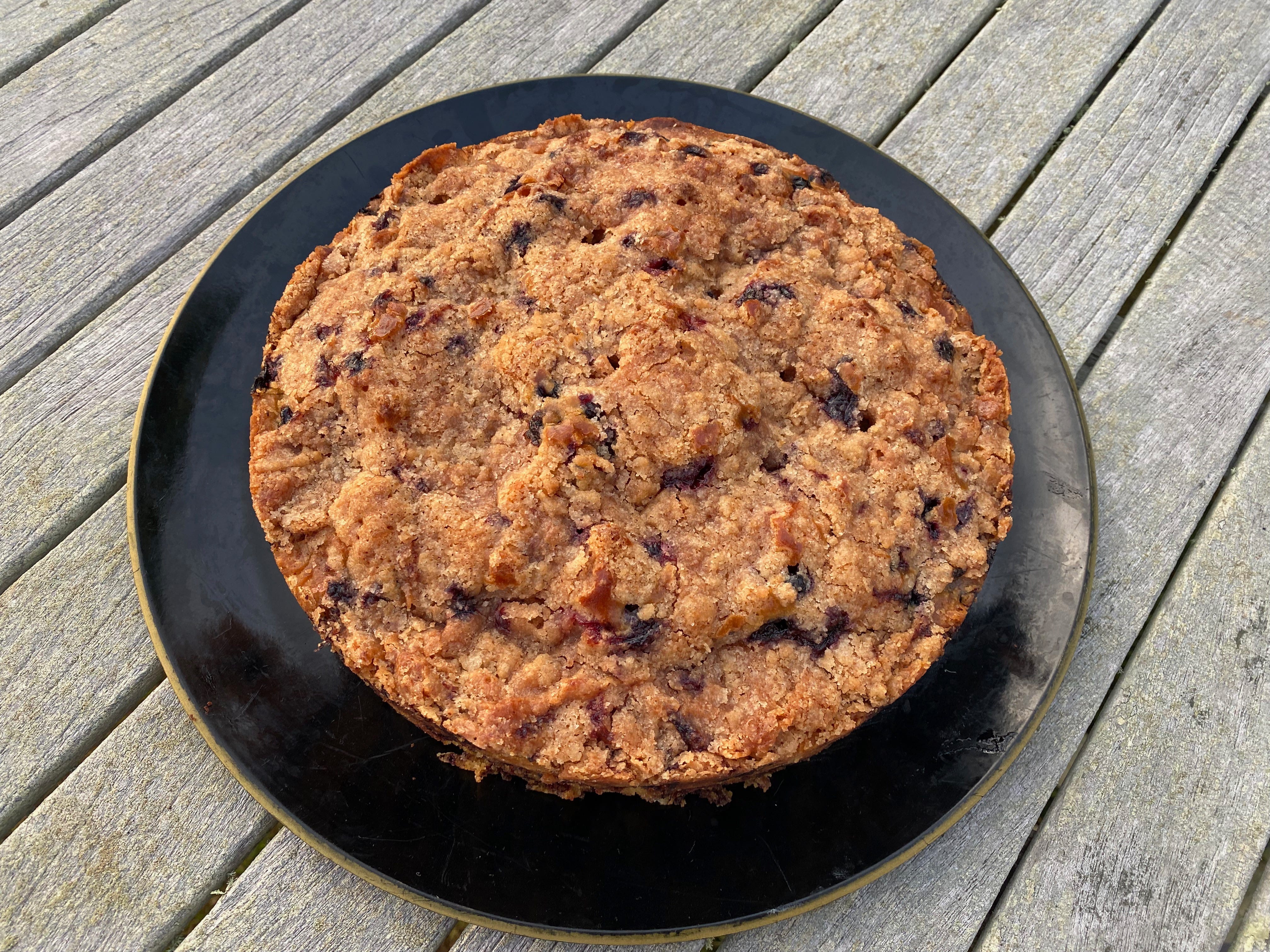 A round blueberry cake topped with crunchy caramelized sugar on a black plate.