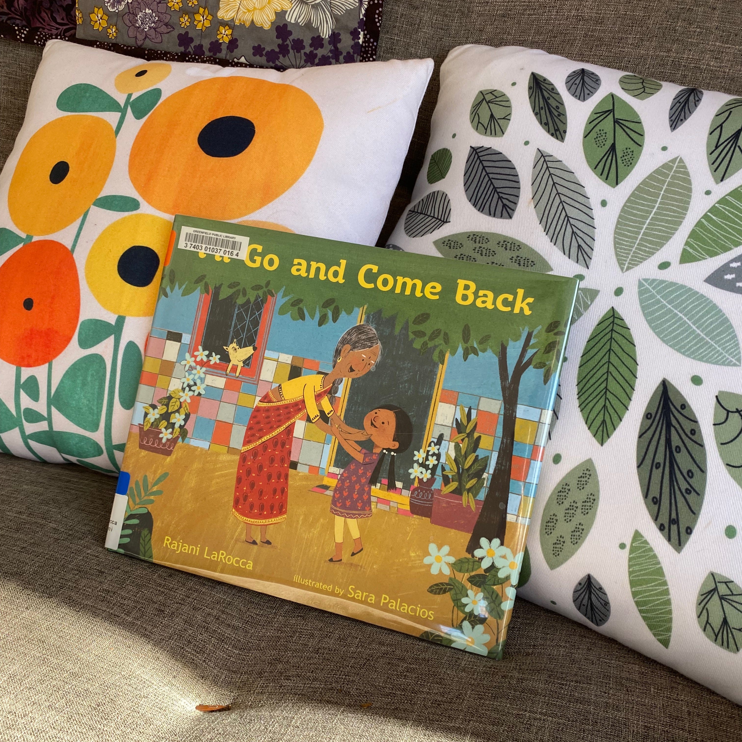 Pictured here leaning against two colorful throw pillows patterned with yellow flowers and green leaves. 