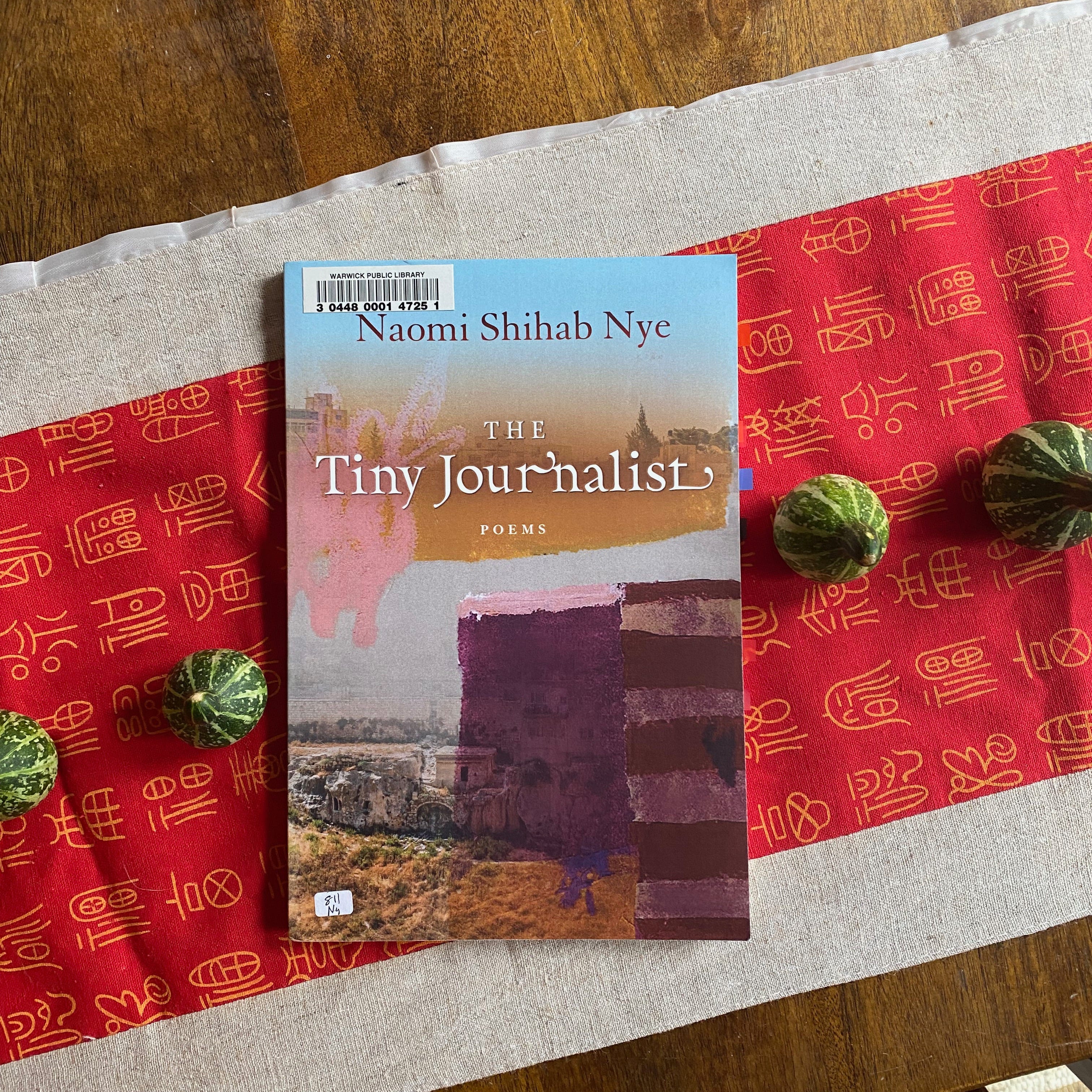 The Tiny Journalist on a red table runner between some tiny gourds.