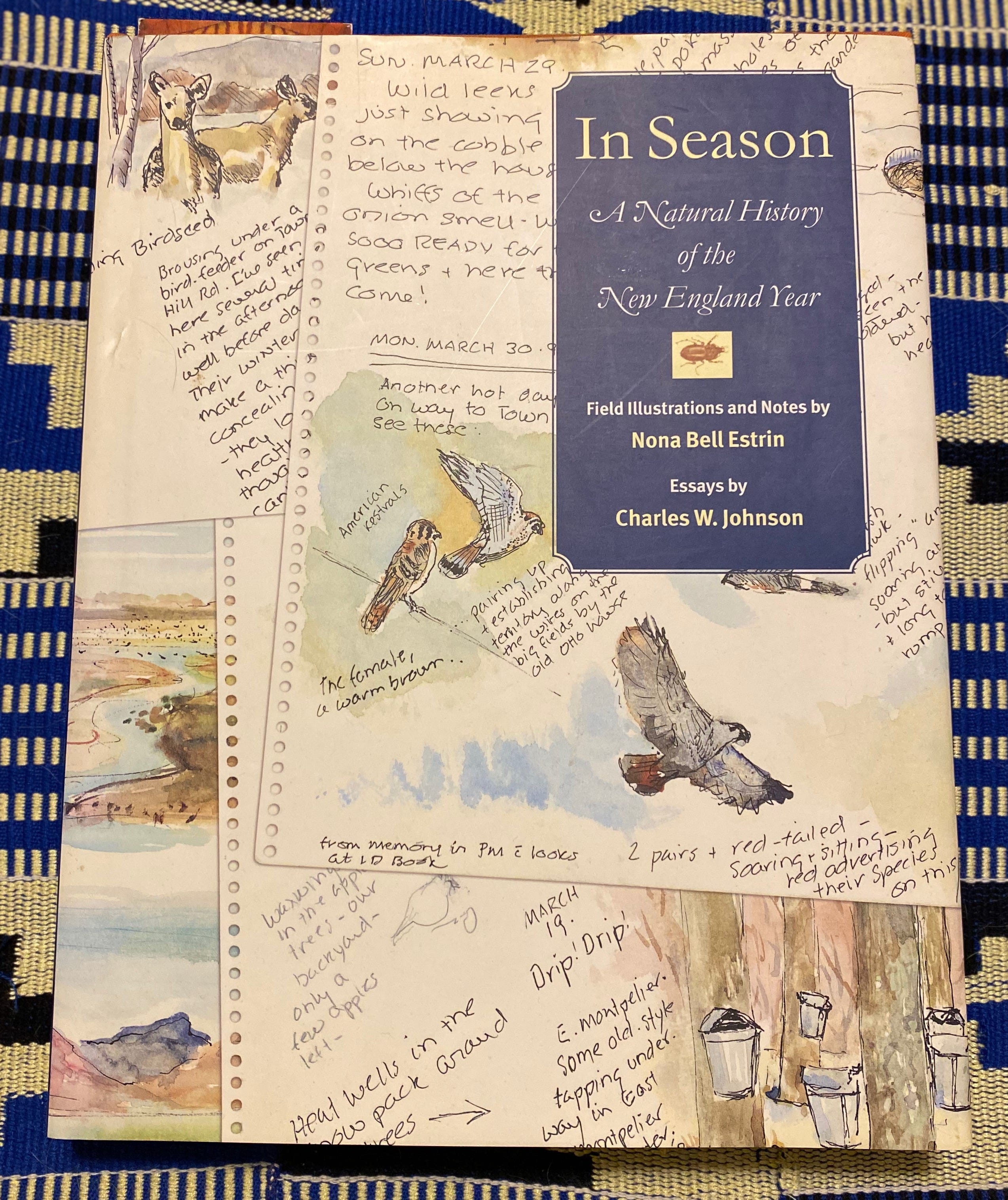 In Season, a large white hardcover with illustrations from a page of field notes, sits o na blue and white cloth.