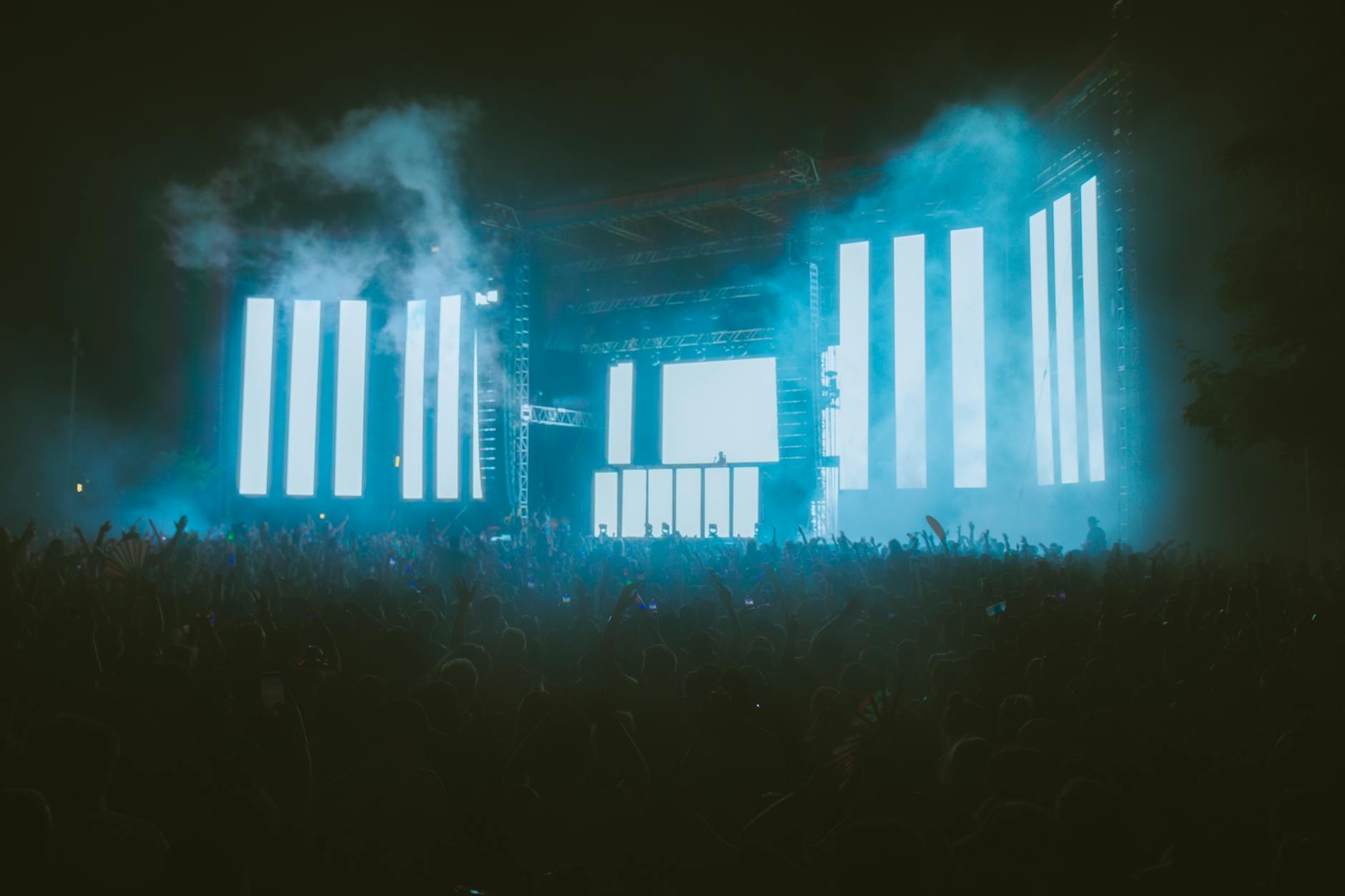Festival crowd with hands raised under huge LED screens and colored stage lights.