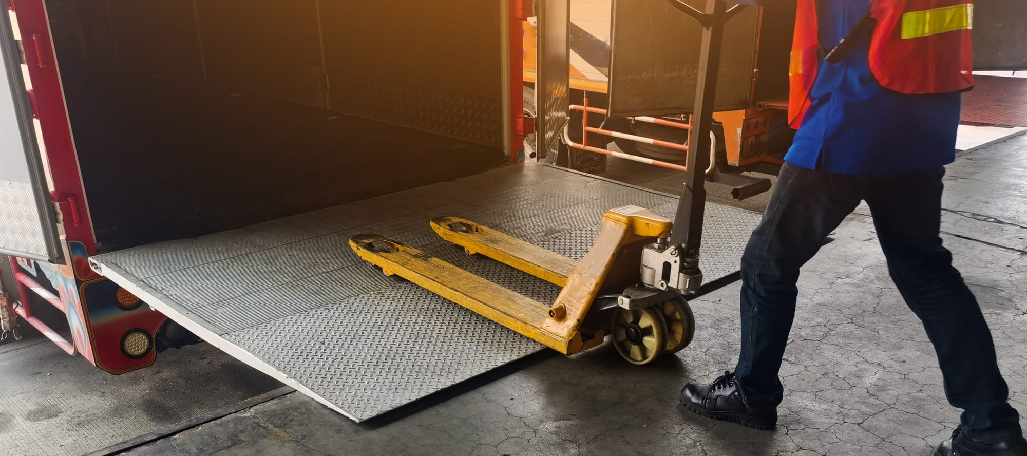 Worker driving forklift loading shipment carton boxes and goods on wooden pallet at loading dock from container truck to warehouse cargo storage