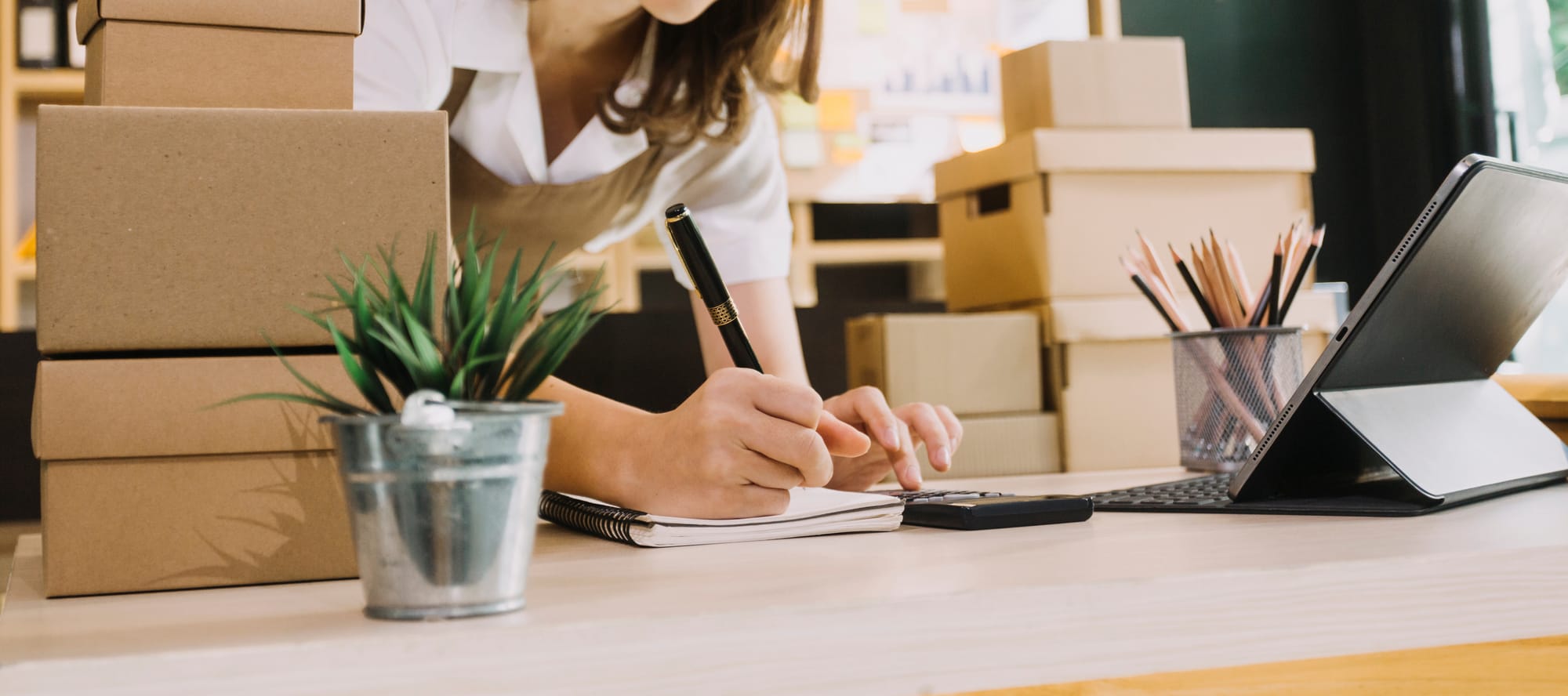 Small business owner with calculator writing on notepad.