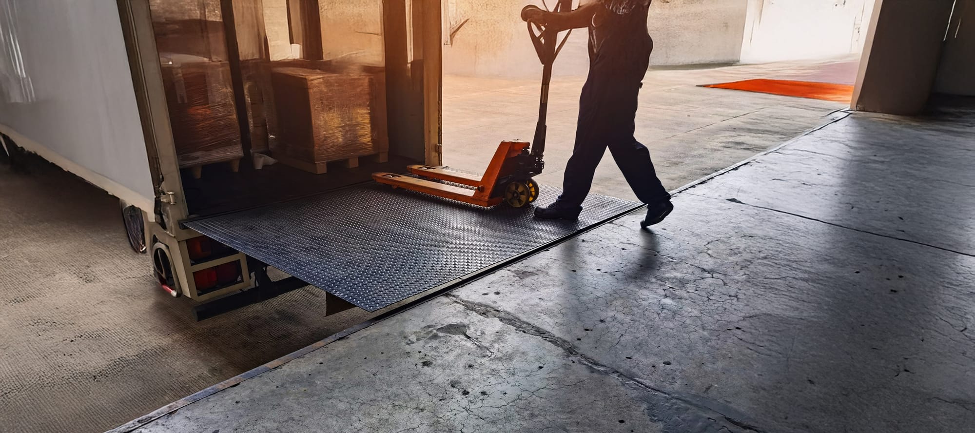 Worker driving forklift loading shipment carton boxes goods on wooden pallet at loading dock to container truck