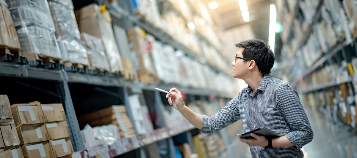Worker doing stocktaking of product in cardboard boxes on shelves in a warehouse.