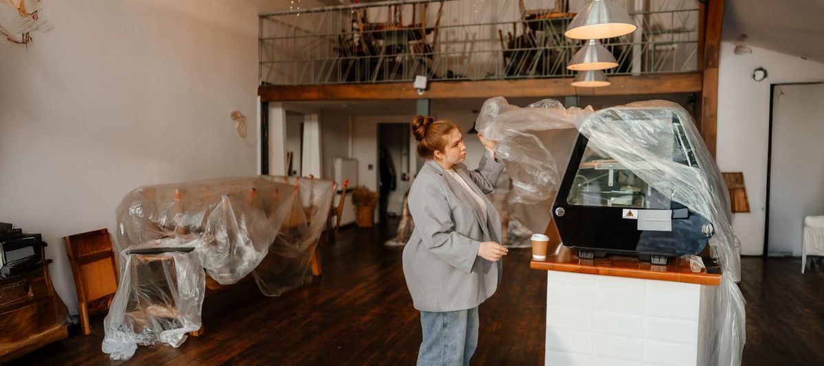Woman cafe owner stands and removes plastic covering from equipment before opening the cafe