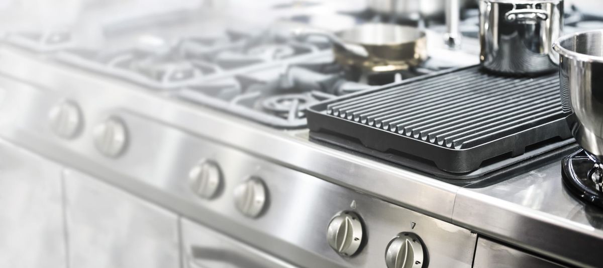 Close up of an industrial oven and cooktop with stainless steel pans.
