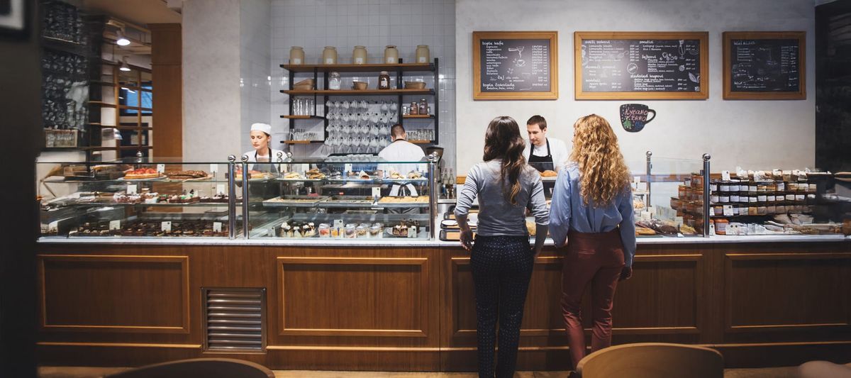 Back view of two young women ordering food at bakery shop. Bakery equipment, bakery shelving, used bakery equipment
