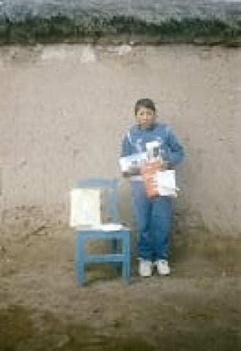 Photo of ChildFund sponsored girl child in front of her adobe-style home, holding items purchased with support