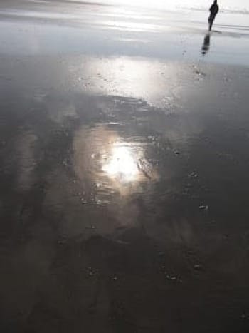 Photo of sun and clouds reflected on wet beach sand