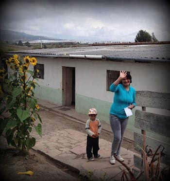 Photo of Ecuadorian mother and her young son, waving good-by in front of their cement and metal-roofed house.