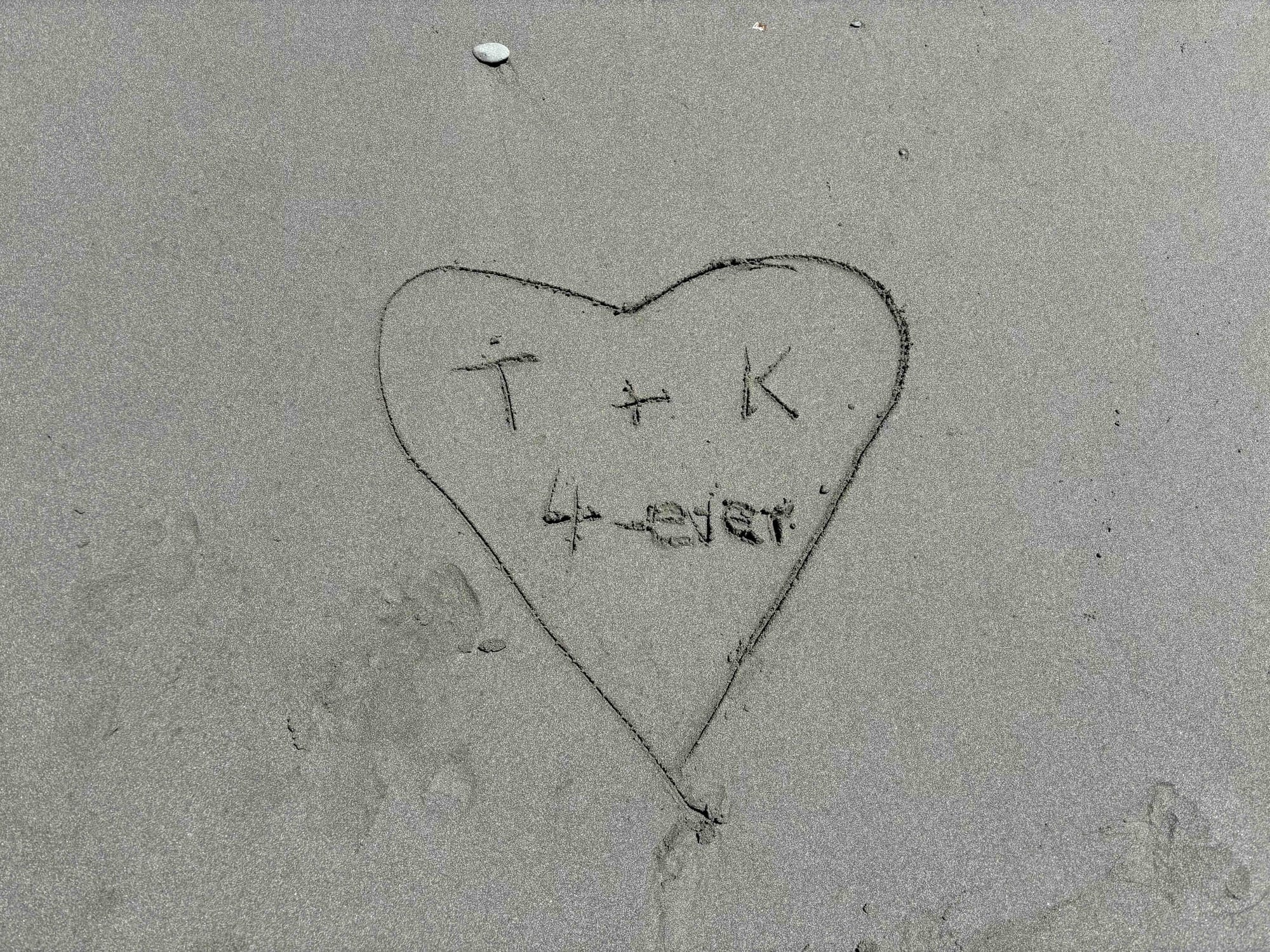Photo of a heart with initials and 4-ever carved in beach sand.