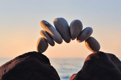 Photo of rocks stacked like a cairn except arcing so that the rocks form a little bridge from one big rock to another by the ocean