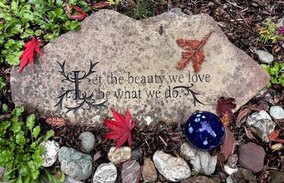 Photo of a carved stone that says, Let the beauty we love be what we do, with stones, and two small Japanese red maple leaves.