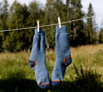 Photo of two, soft blue socks hanging on a clothesline with woods behind.