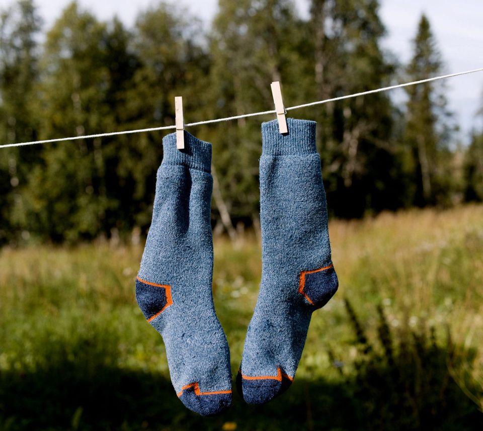 Photo of two, soft blue socks hanging on a clothesline with woods behind.