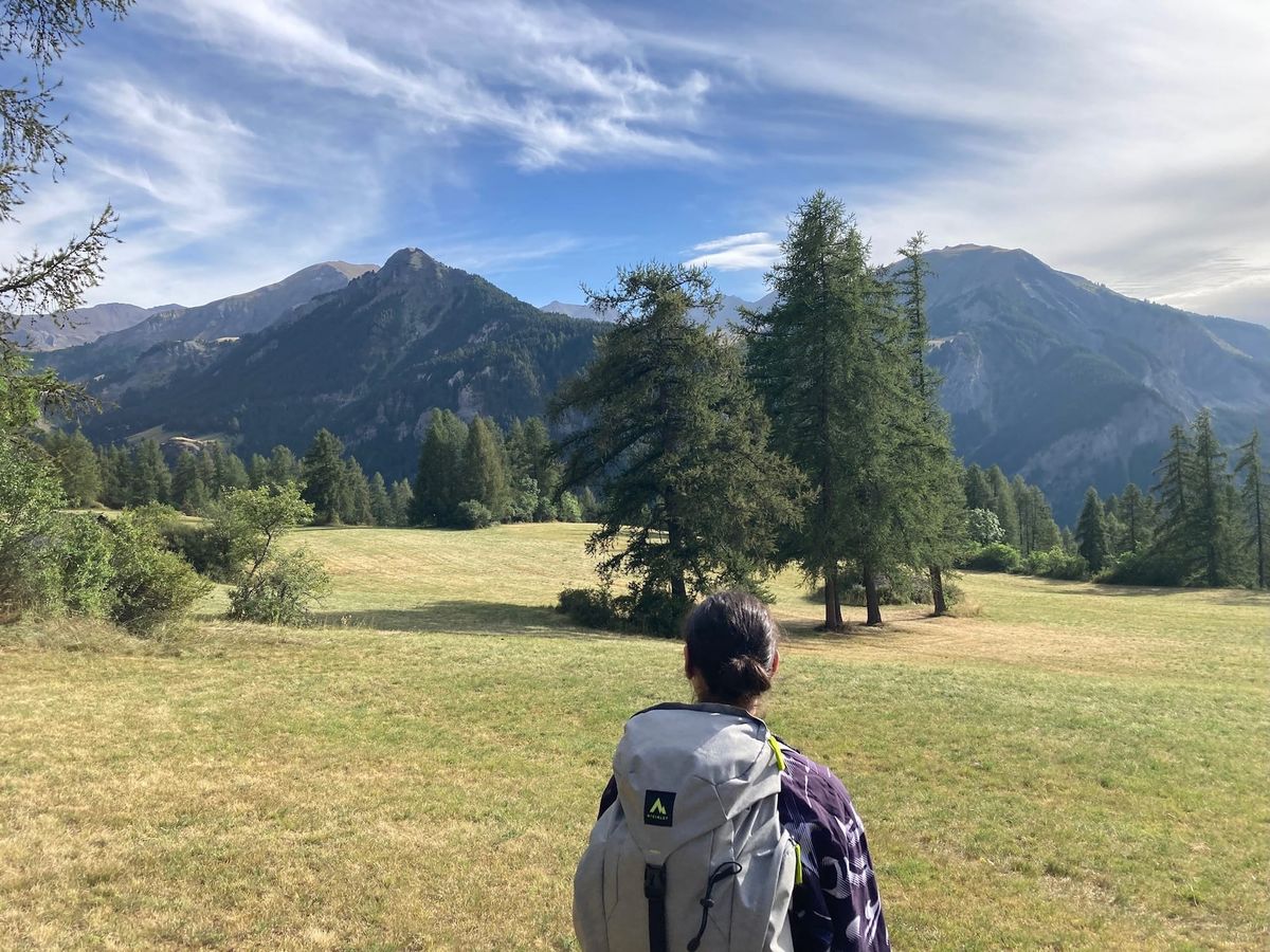 The author, wearing a hiking backpack, standing in an alpine meadow overlooking mountains in the French Alps