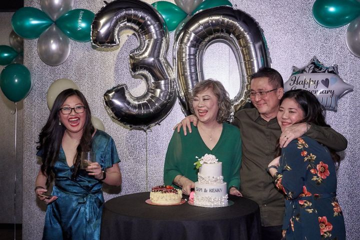Brenda’s mum laughing at her 30th anniversary party, surrounded by family, silver “30” balloons, and two celebratory cakes.