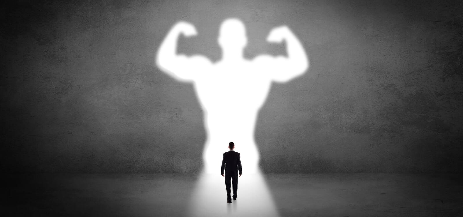 Man in suit walking toward a shadow of a large man showing off his biceps