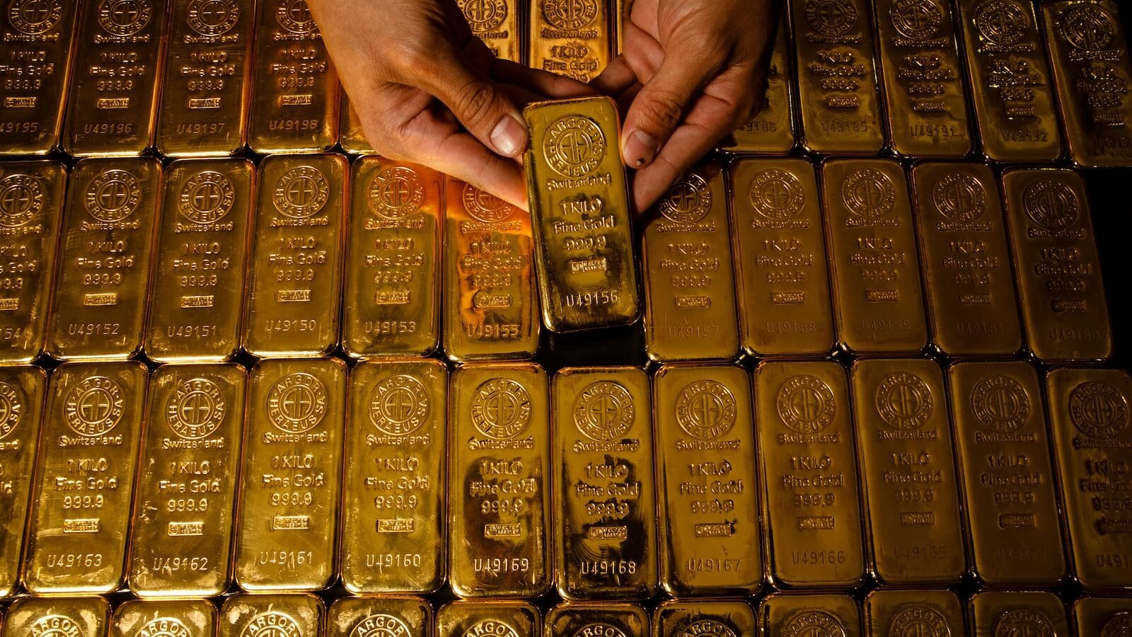 Person lifting gold bar from a stack: gold is breaking out again