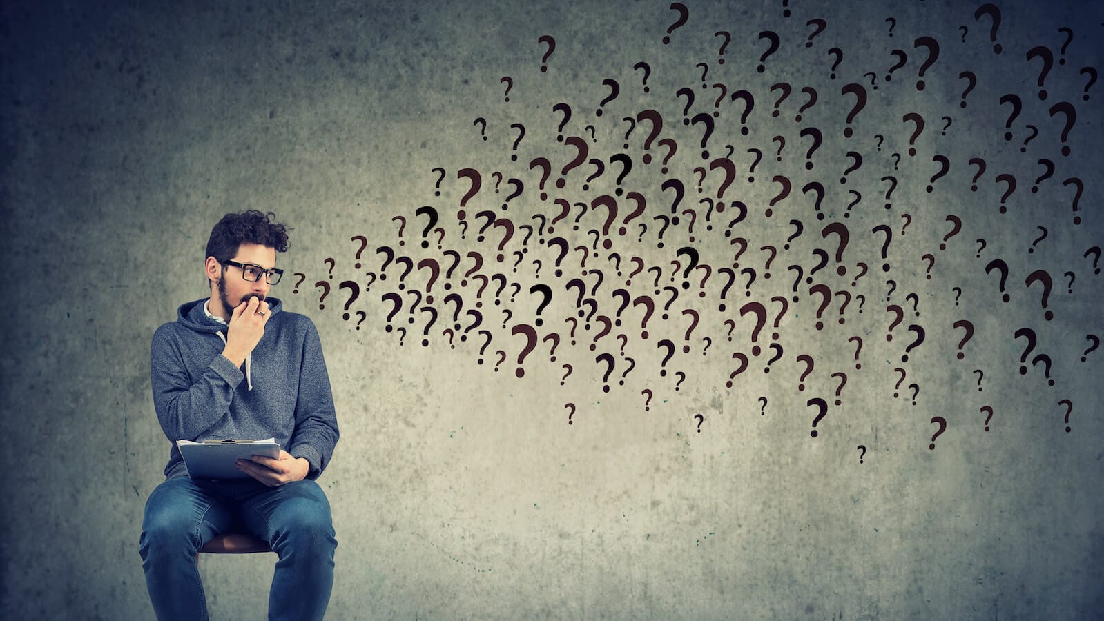 Man sitting on chair with clipboard several question marks: September scaries in stock market