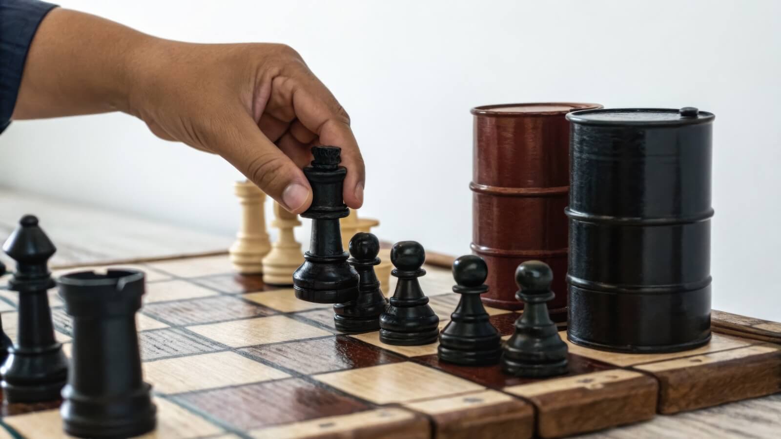 hand moves black king chess piece on chessboard next to two black and brown oil barrels