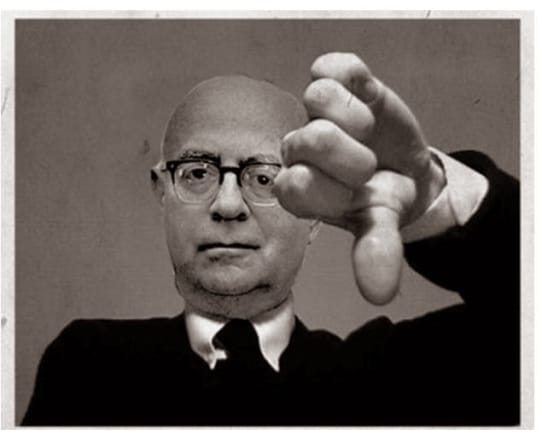 A balding white man in glasses presents a downward pointing thumb.