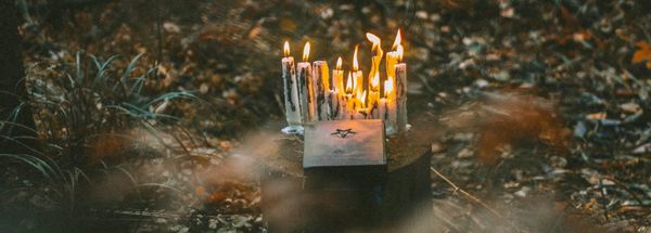 A photo of some lit candles and a paper with a star on it set out as an offering on a tree stump.