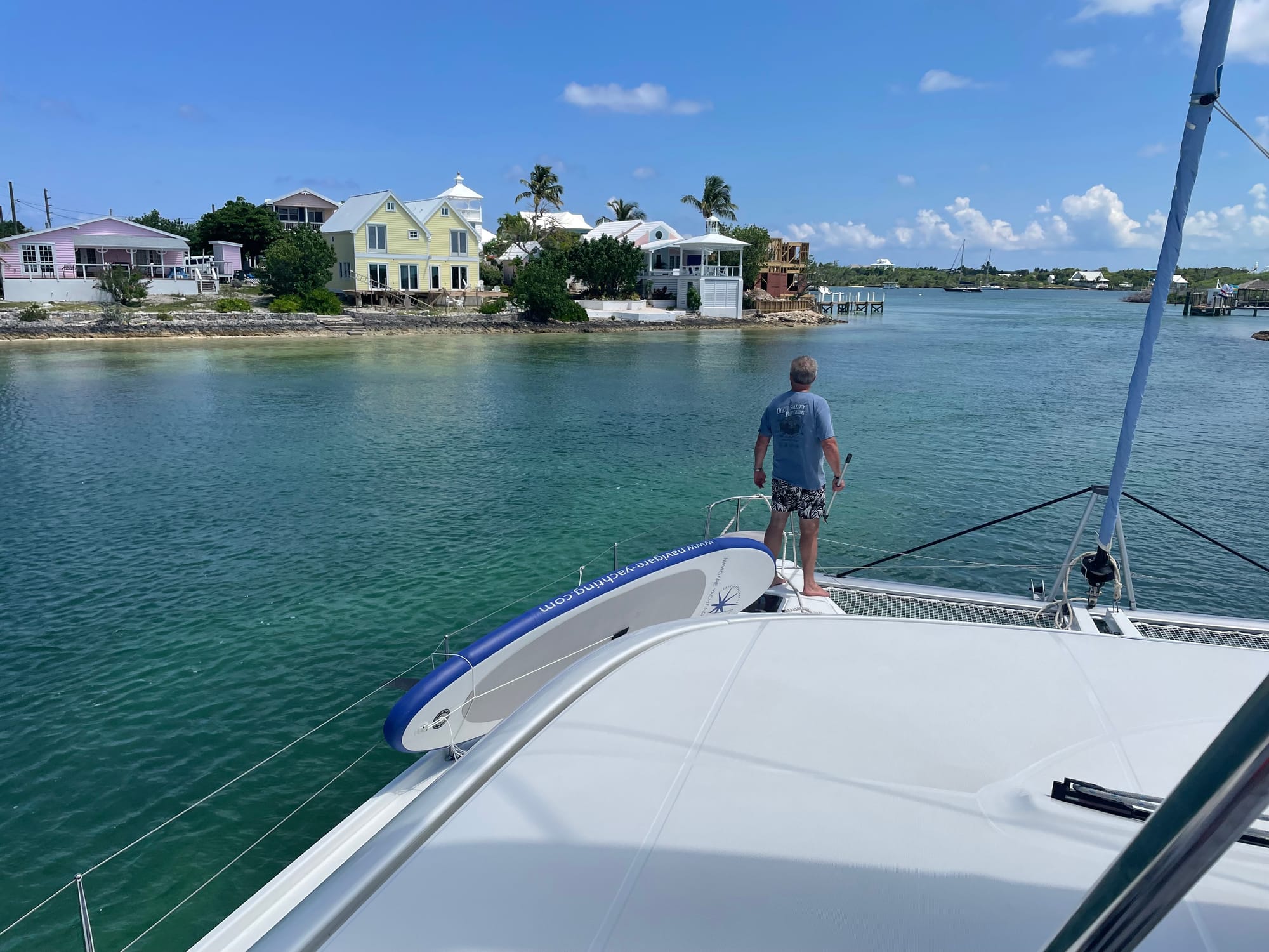 Person standing at front of a catamaran with boathook in hand