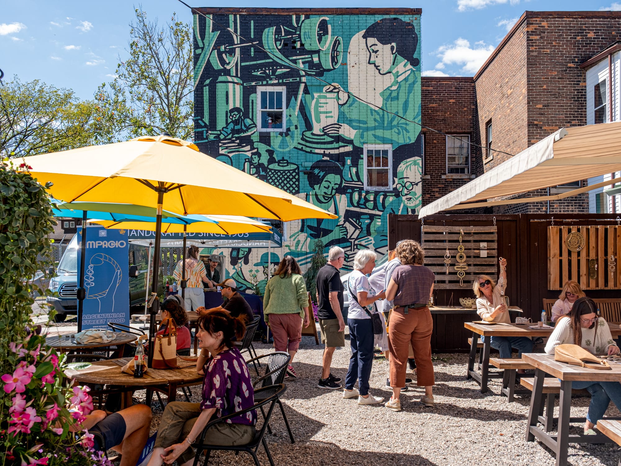 A group of people stand outside and congregate in the blue mutual stand in the background behind it. 