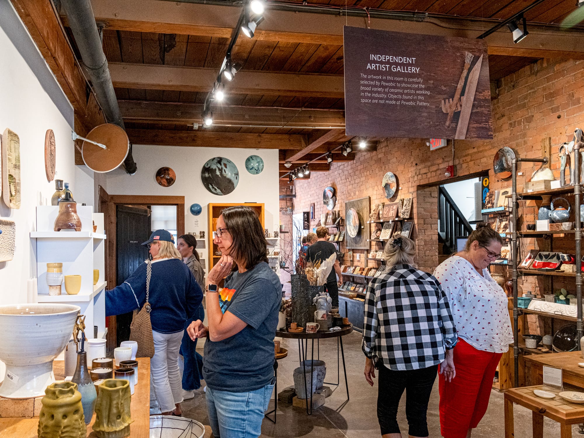 People browse inside of a room that has walls and tables filled with different types of ceramics.   