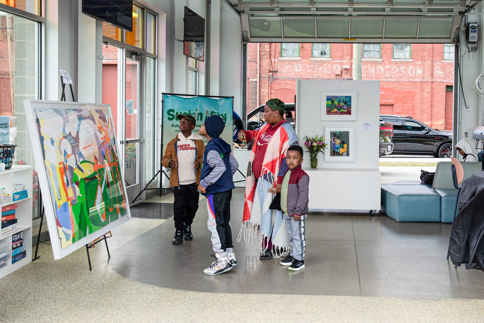 A group of four people, look at a large colorful painting displayed on an easel inside an art gallery.
