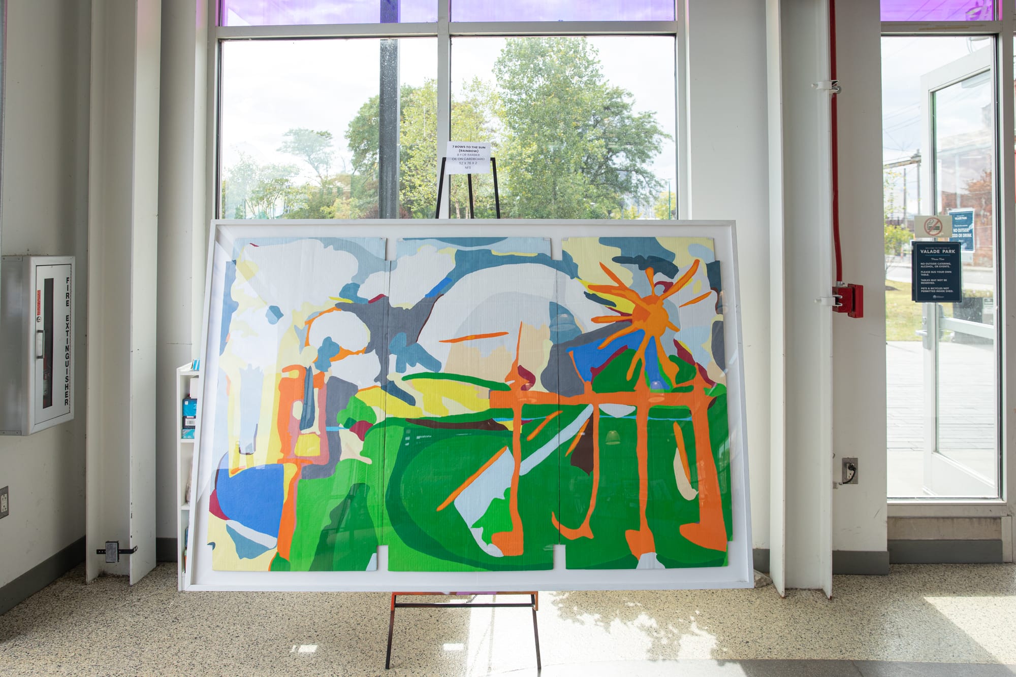 An abstract painting with layered colors and shapes displayed on an easel inside a modern gallery space.