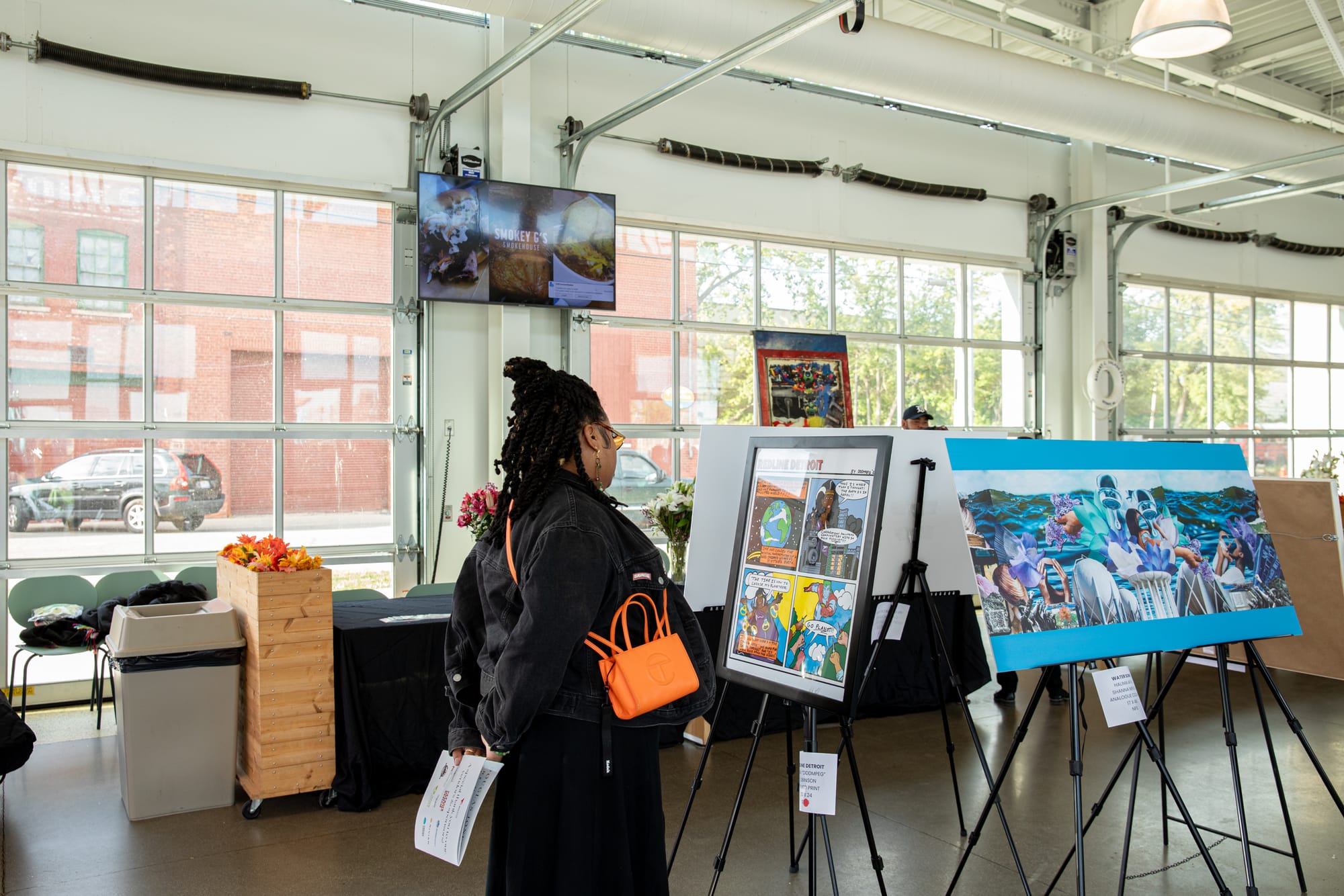 A woman looks at artwork on an easel surrounded by other artworks in an exhibition space.