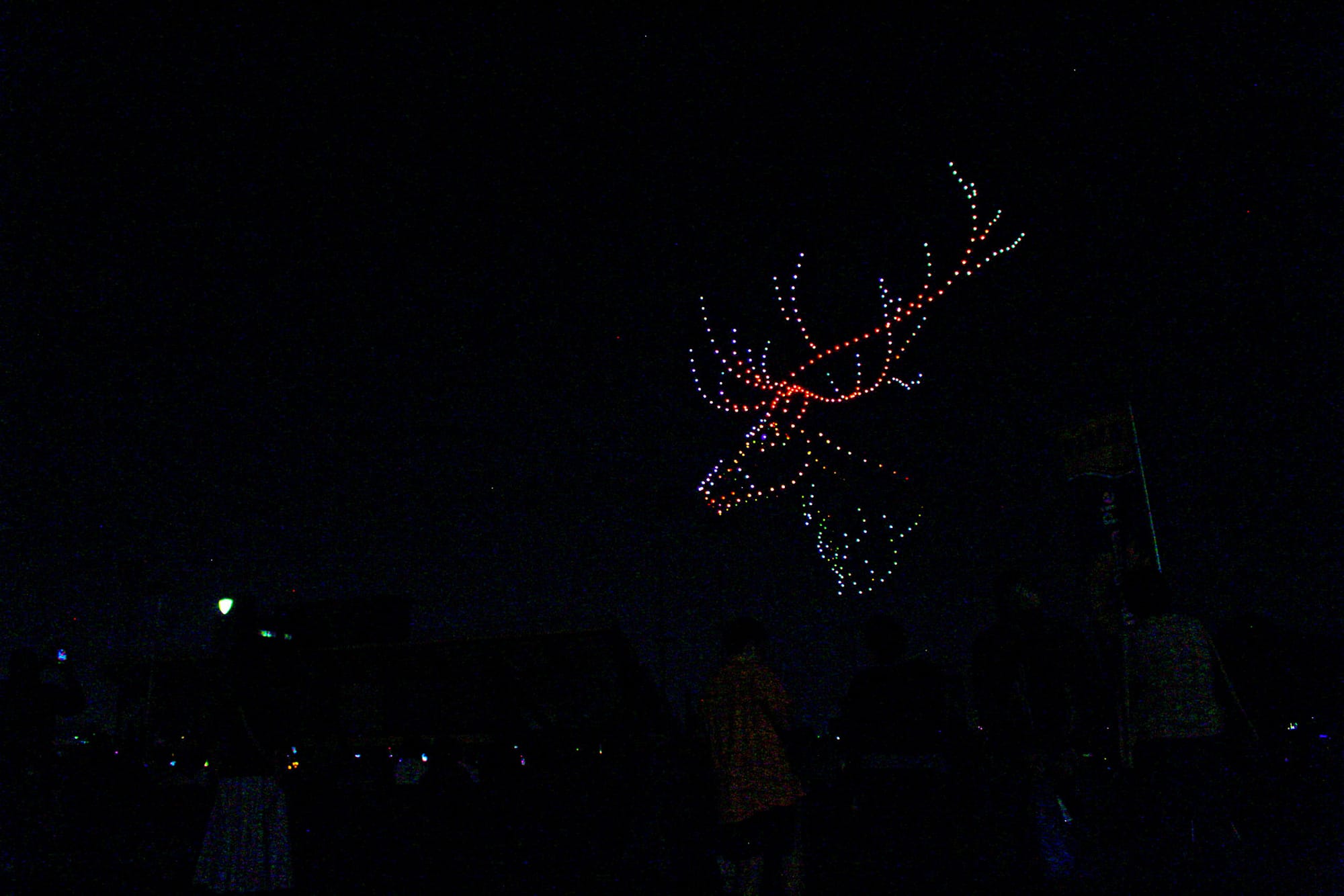 Hundreds of drones form a giant deer head with antlers made up of reds, greens, and blues.