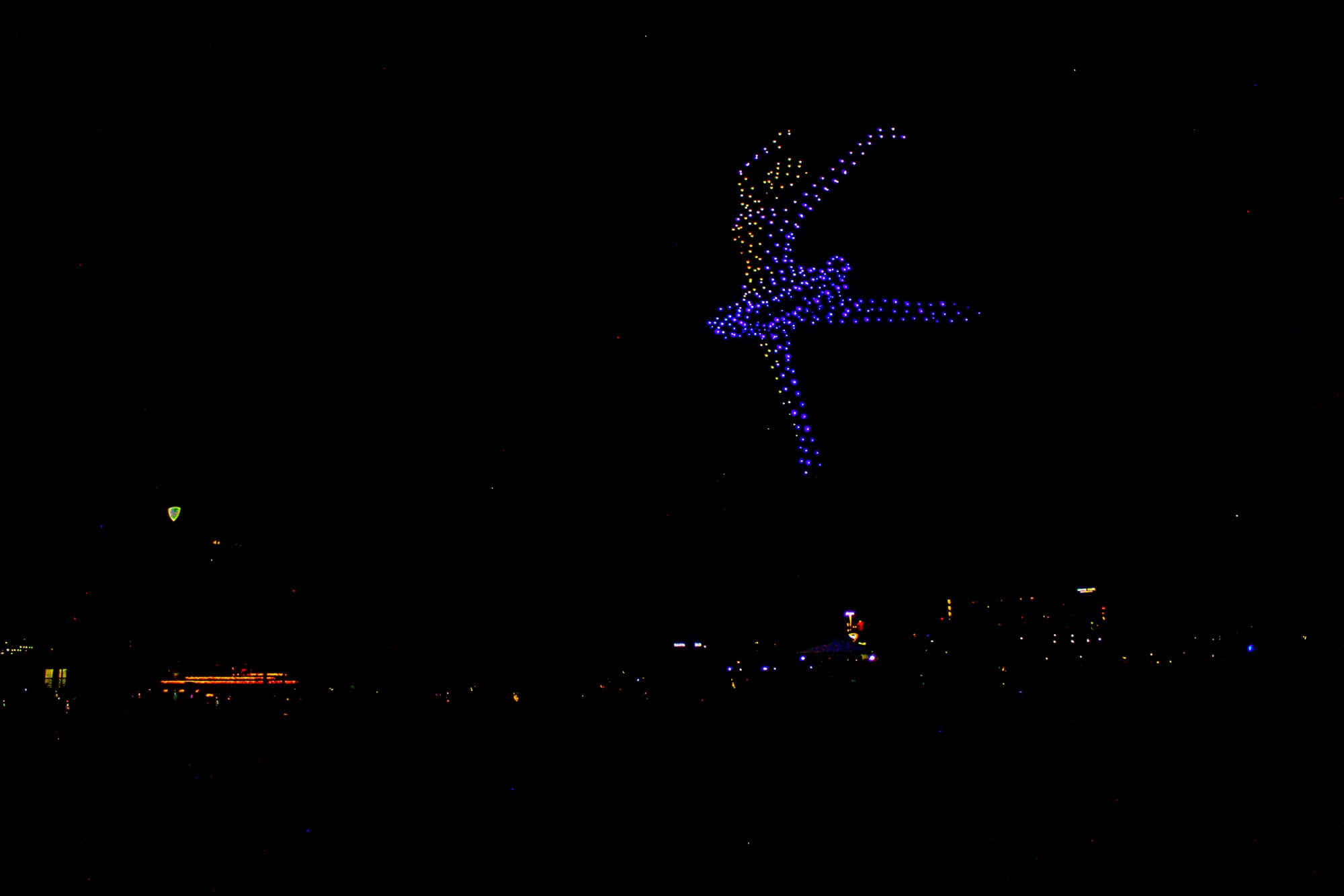 Hundreds of drones light up the night sky with a blue and yellow ballerina dancing with her arms in the air and one leg up.