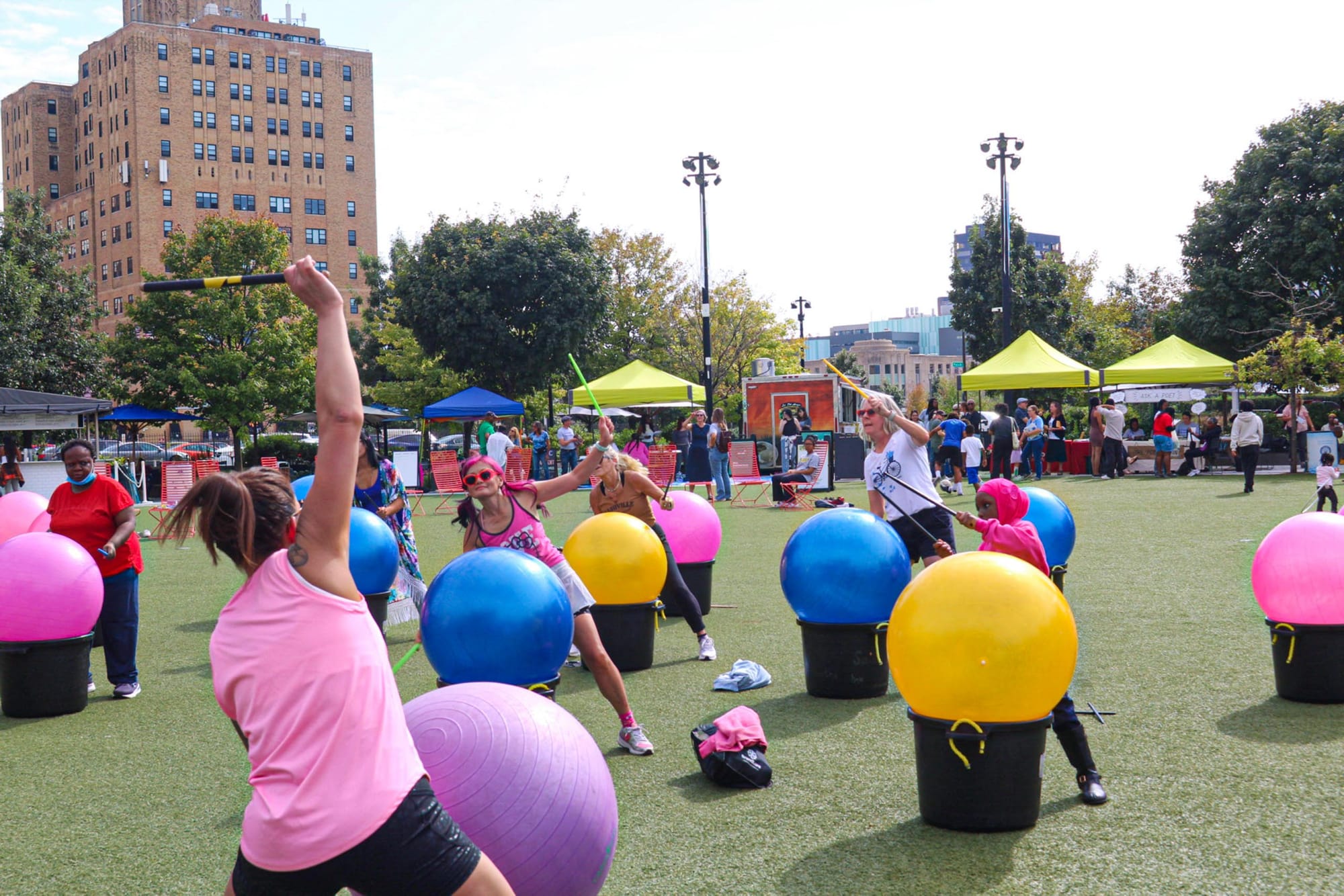 A group of people performing a unique exercise where they beat on exercise balls with sticks like a drum as a way to mix music and cardio.