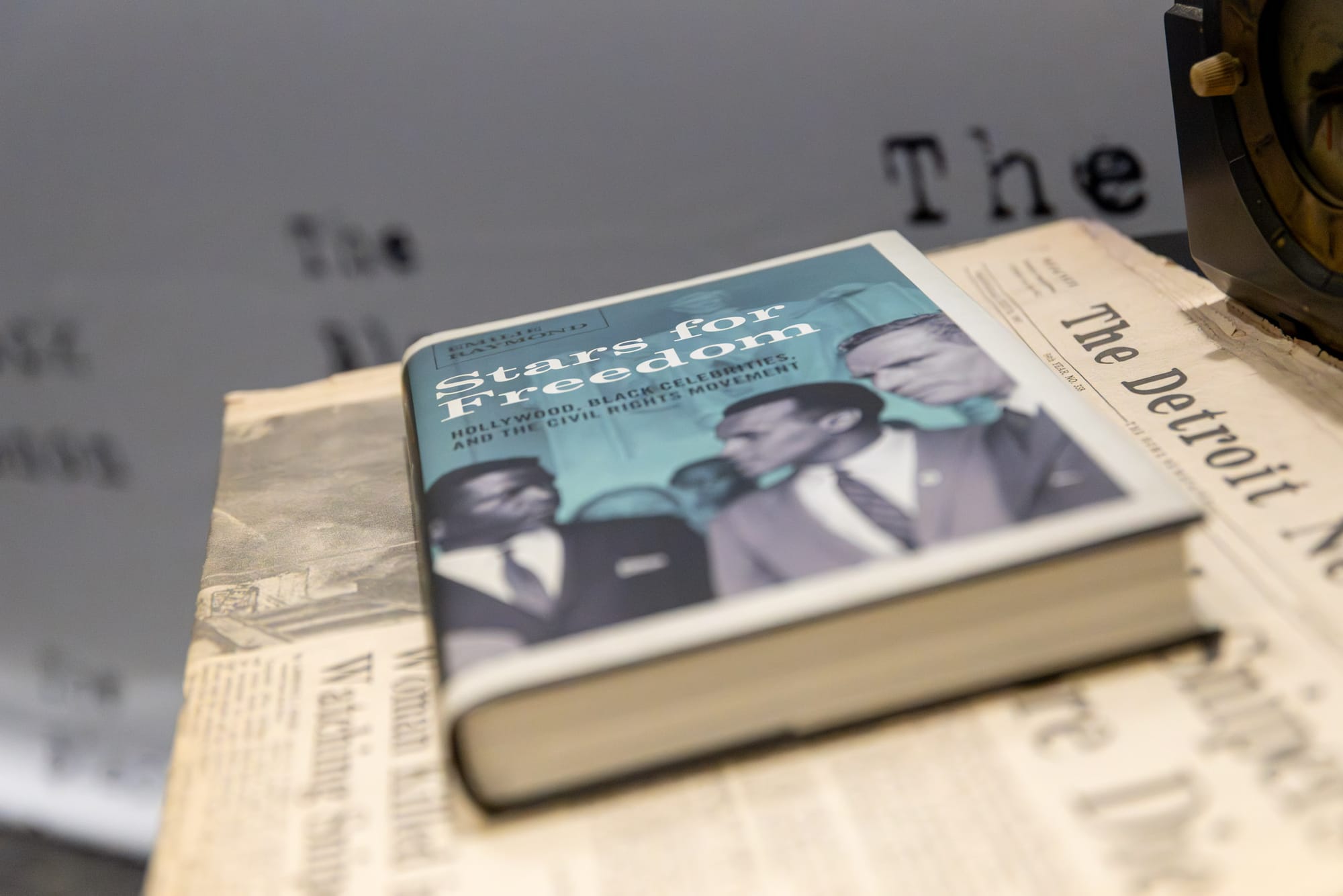 A book sits on top of a newspaper and in the background there is a white backdrop that reads “Black Canon.”