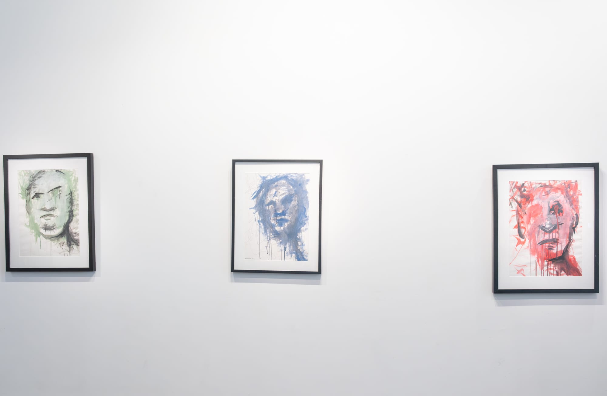 Against a white wall, three paintings are displayed, each distinguished by its own color: green, red, and blue.