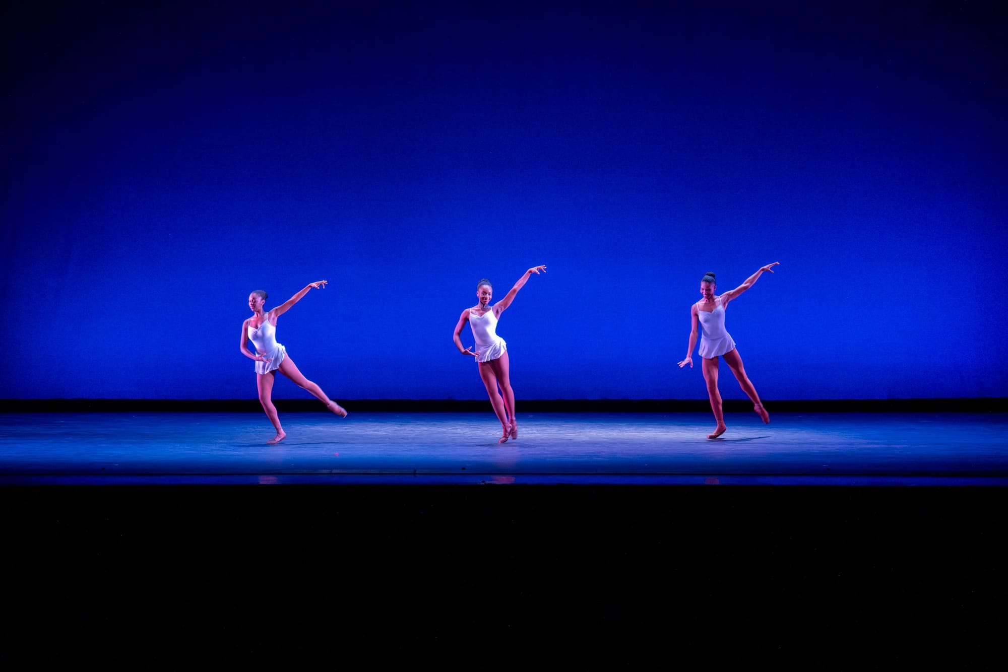 Three dancers jump into the air in front of a blue screen in the background.  